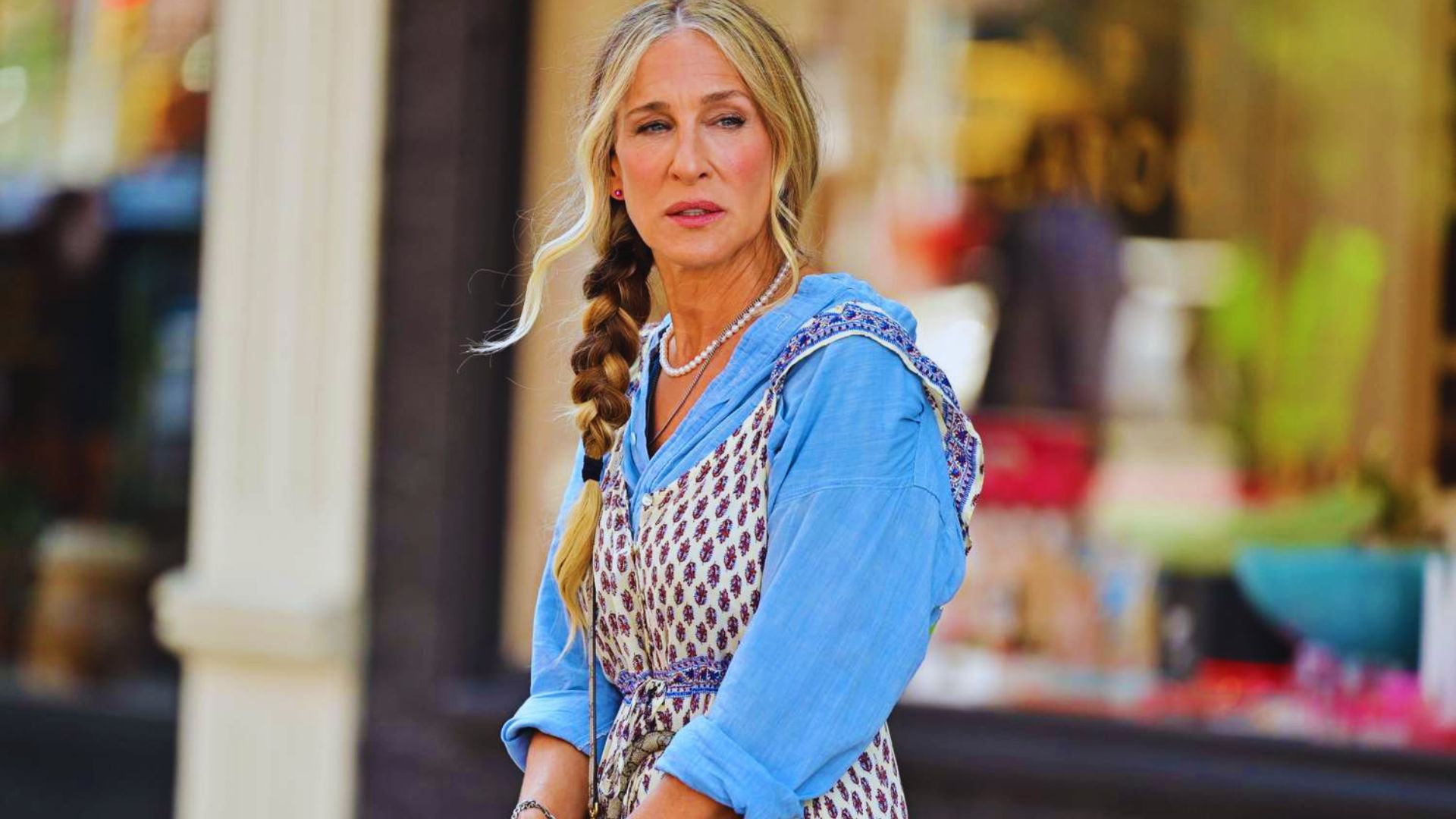 A woman with a braid walks down the street, dressed casually and enjoying her surroundings.