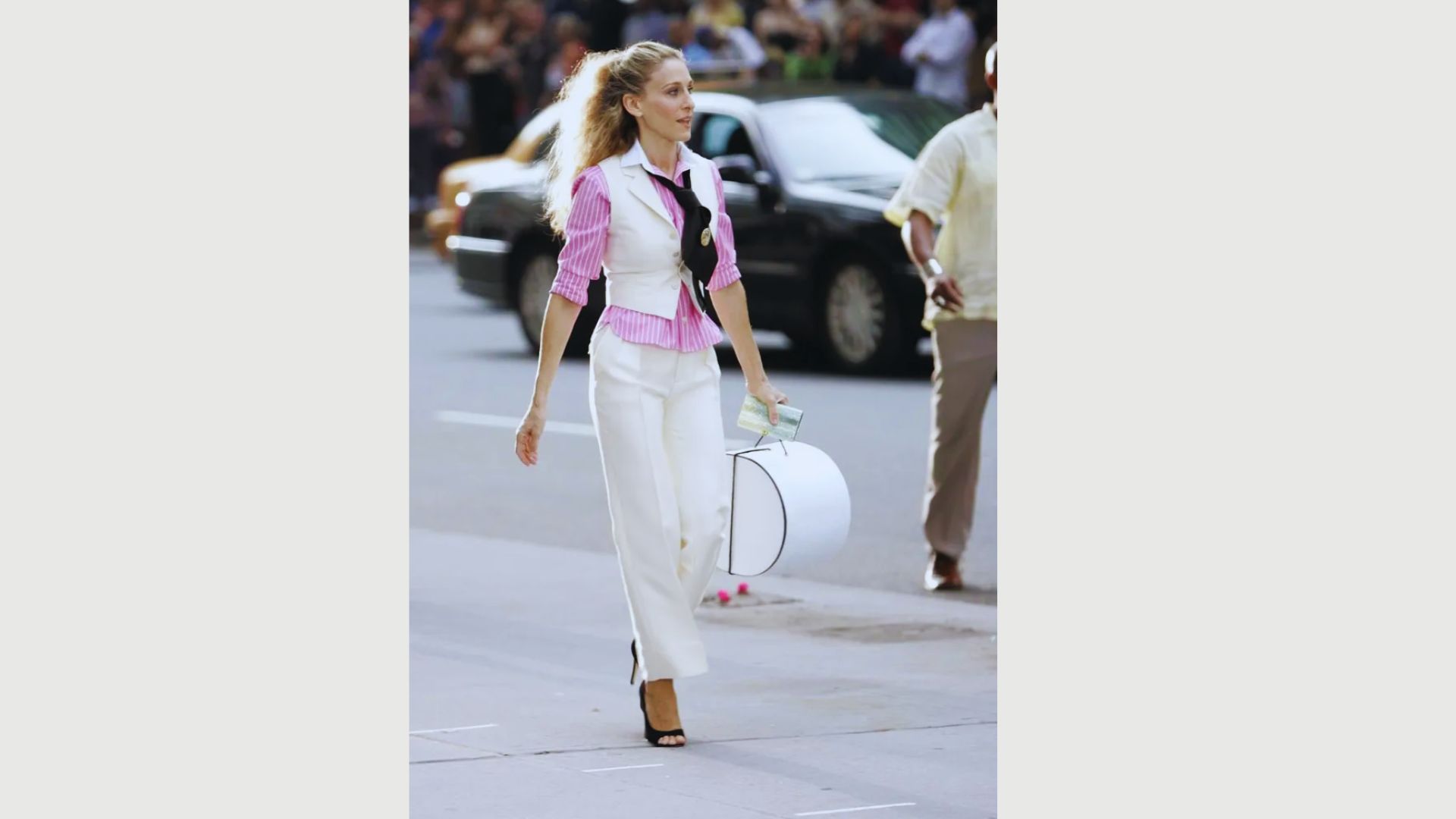 A woman wearing white pants and a pink shirt walks casually on the sidewalk.