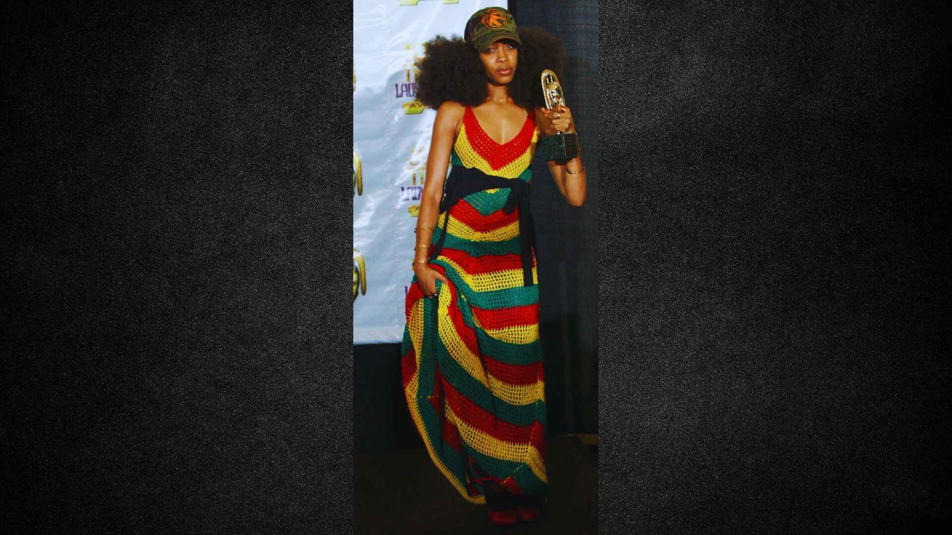 A woman in a vibrant dress stands holding a microphone, ready to speak or perform.
