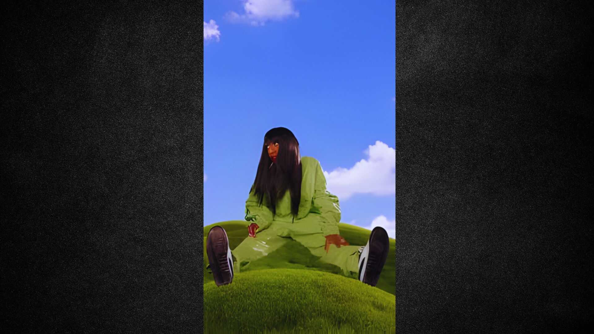 A woman sitting on a lush green hill, enjoying the view under a clear blue sky.