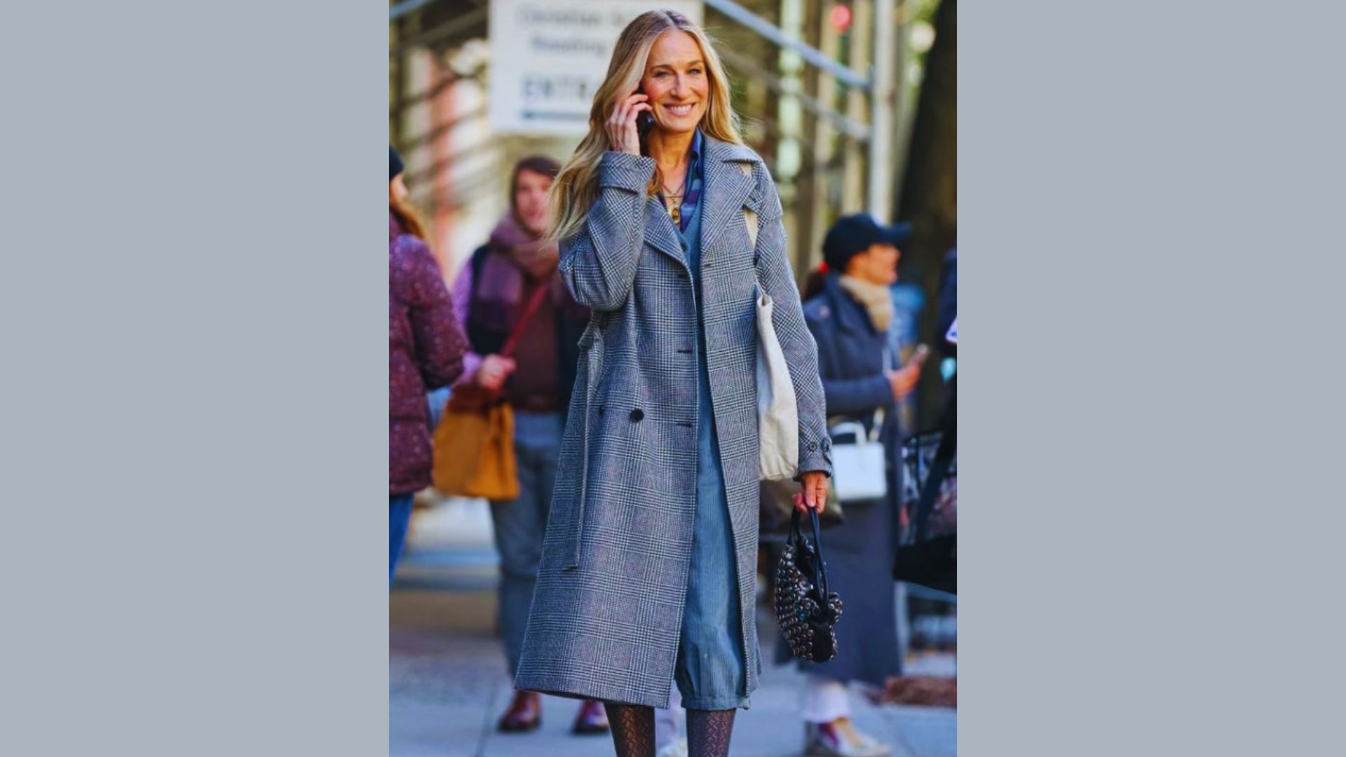 A woman in a gray coat is speaking on her phone, appearing focused and engaged.