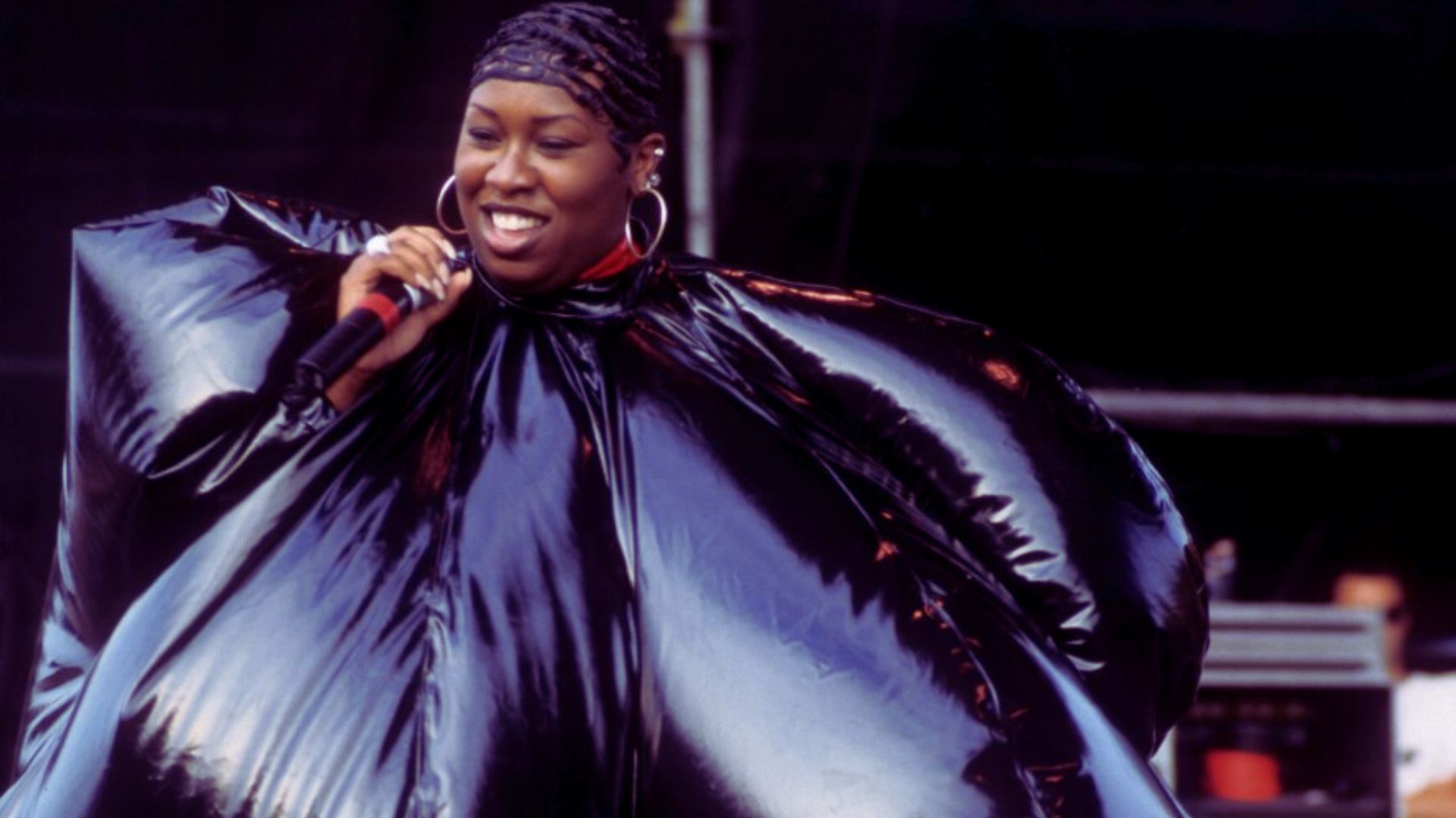 A woman dressed in black stands with a microphone, ready to address an audience.