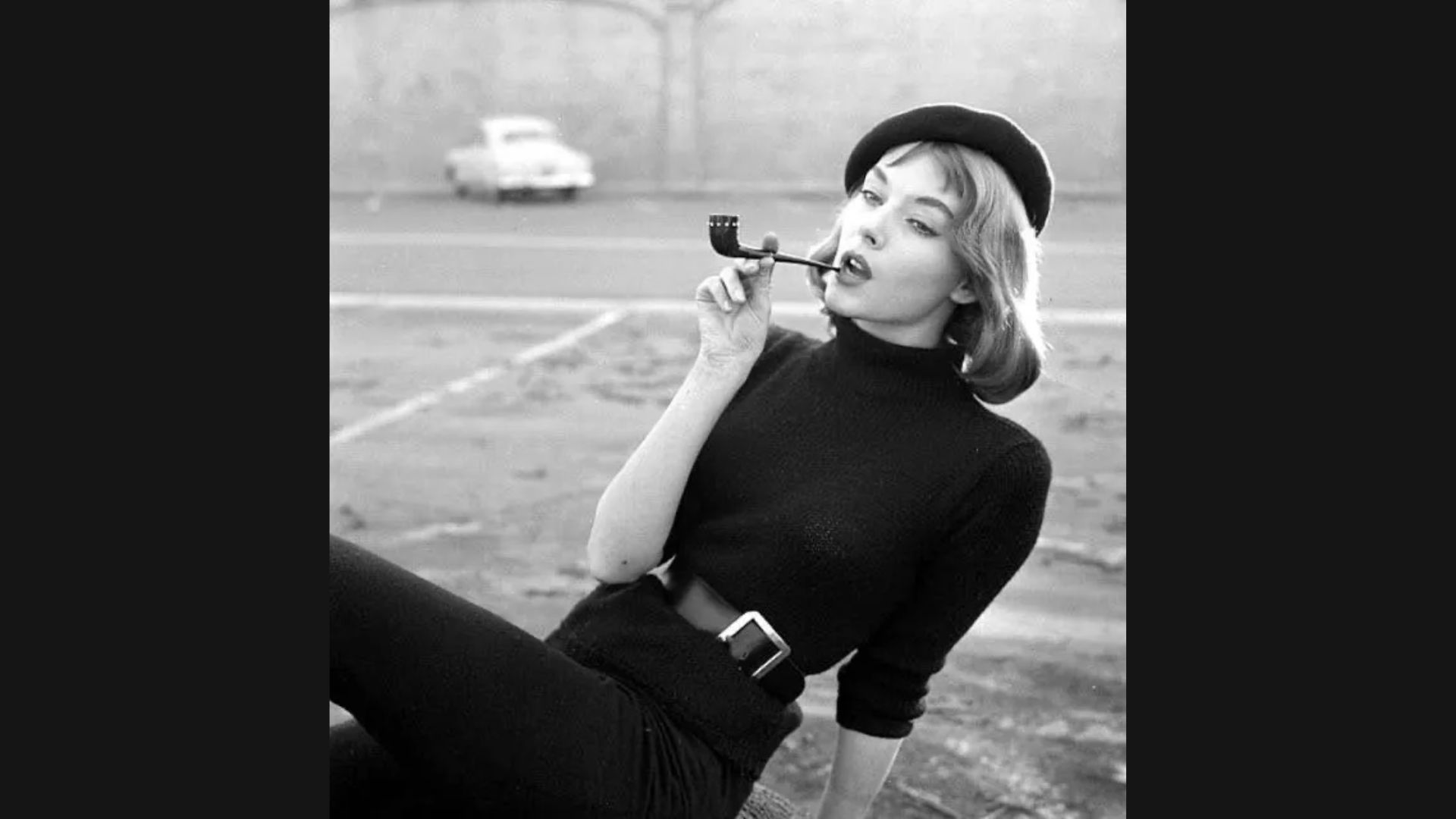 A woman wearing a black top is smoking a cigarette, exhaling smoke in a relaxed manner.
