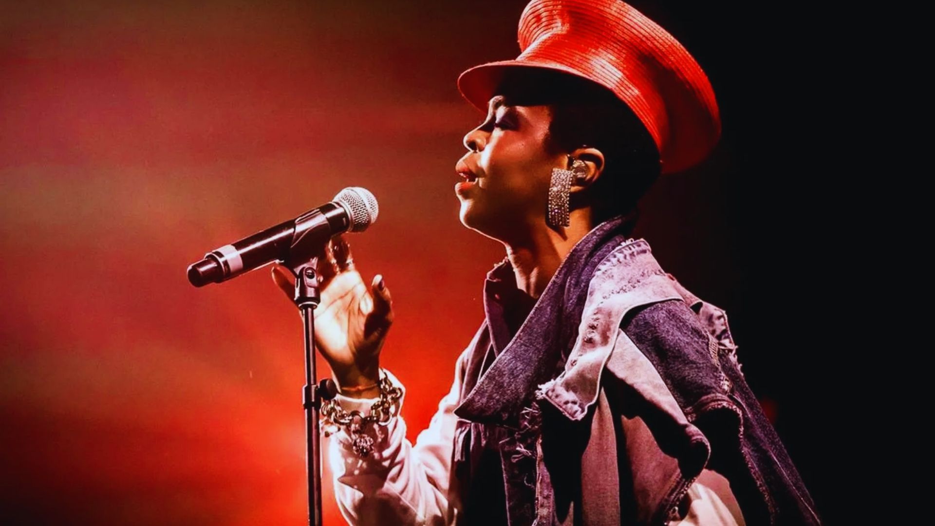 A woman with a red hat is singing into a microphone, engaging the audience with her performance.