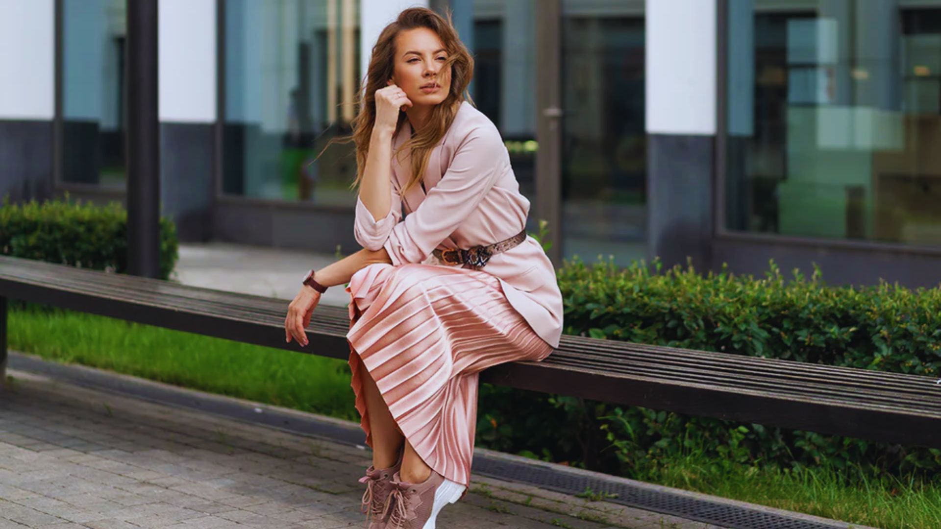 A woman in a pink dress sits on a bench, enjoying a moment of relaxation in a serene outdoor setting.