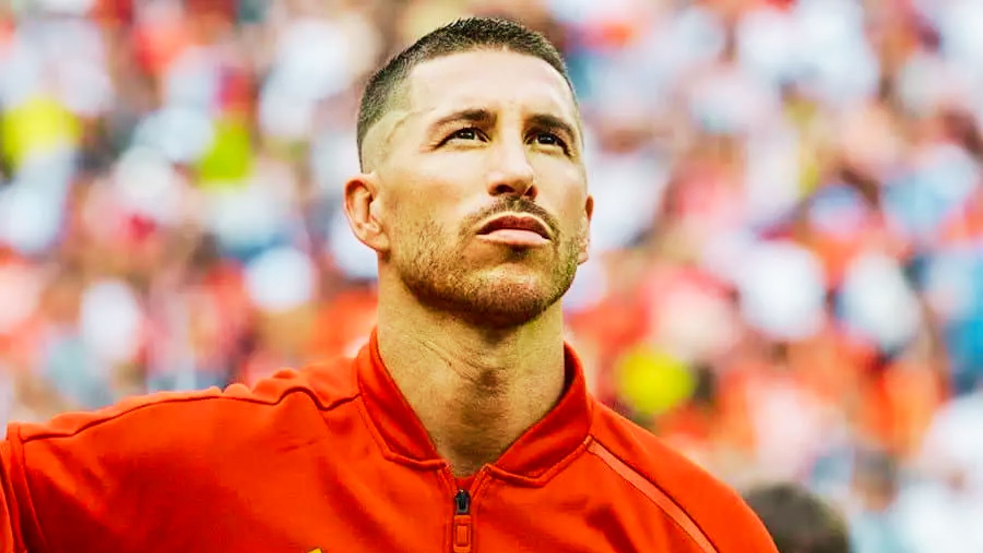 Sergio Ramos in a red shirt with a fade haircut looks thoughtfully to the side, showcasing his stylish hairstyle.