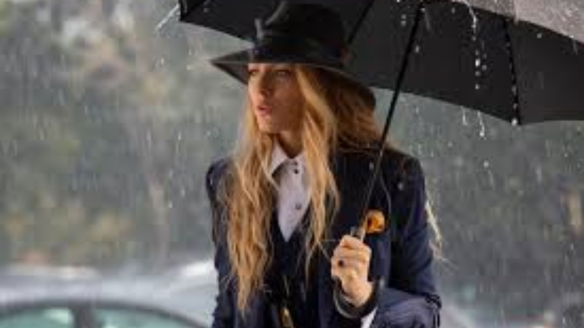 "A woman in a suit and hat walks confidently through the rain, holding an umbrella to shield herself from the downpour."