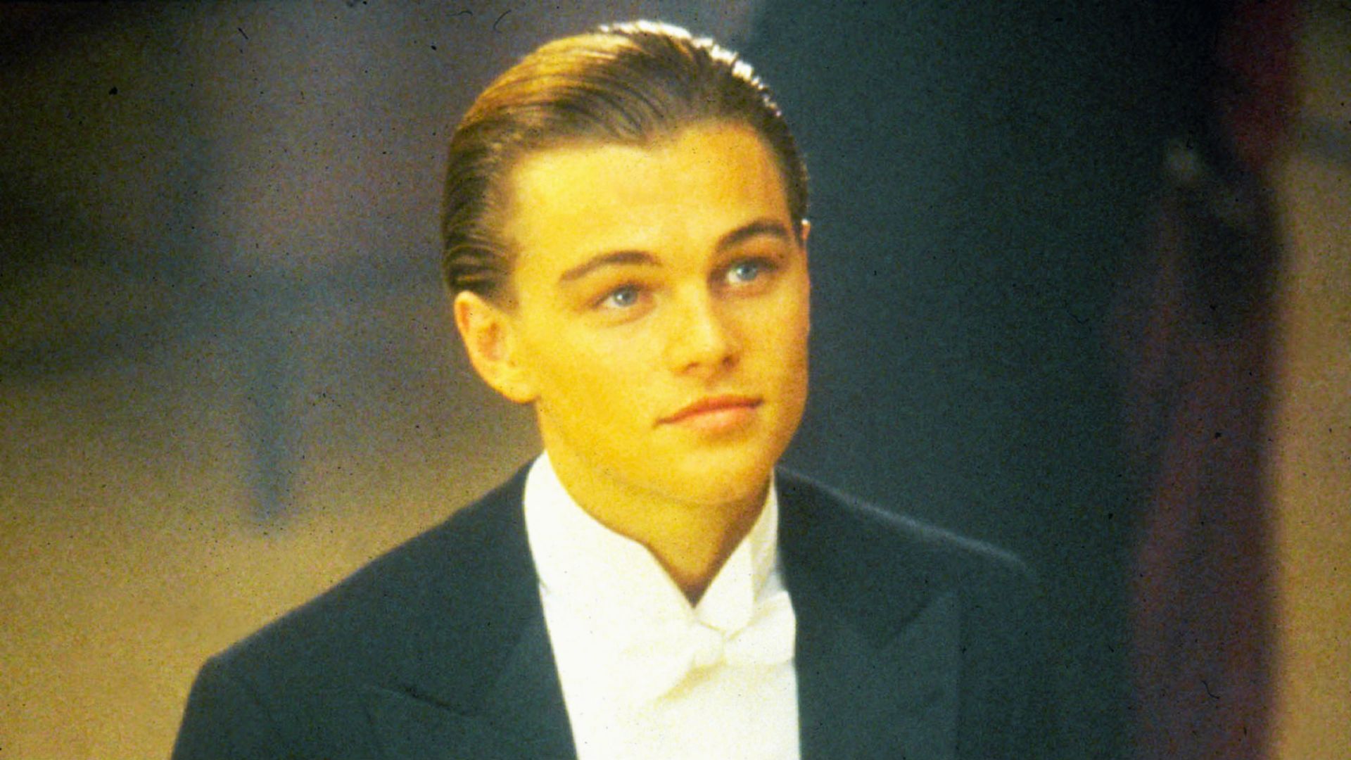 Leonardo DiCaprio as Jack in Titanic wearing a tuxedo and white bow tie. His hair is tightly slicked back in a formal, vintage style for the first-class dinner scene.