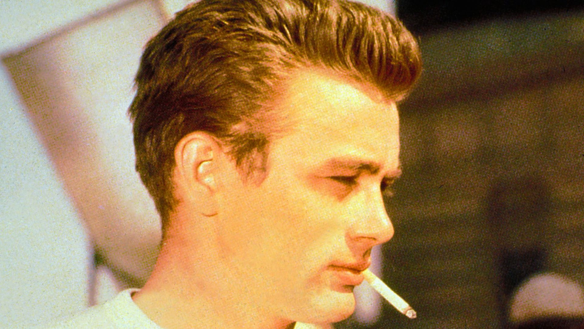 James Dean with a cigarette in his mouth, showcasing the classic hairstyle in a stylish pose.