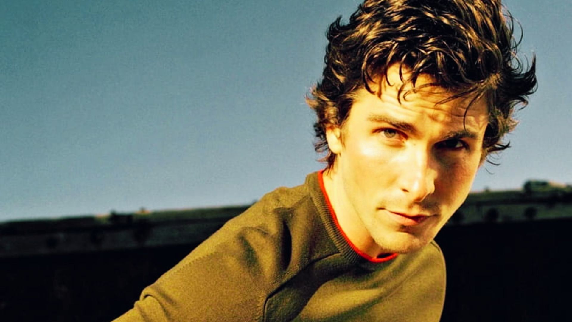 A young man with curly hair poses for a photo, showcasing a hairstyle reminiscent of Christian Bale's early looks.