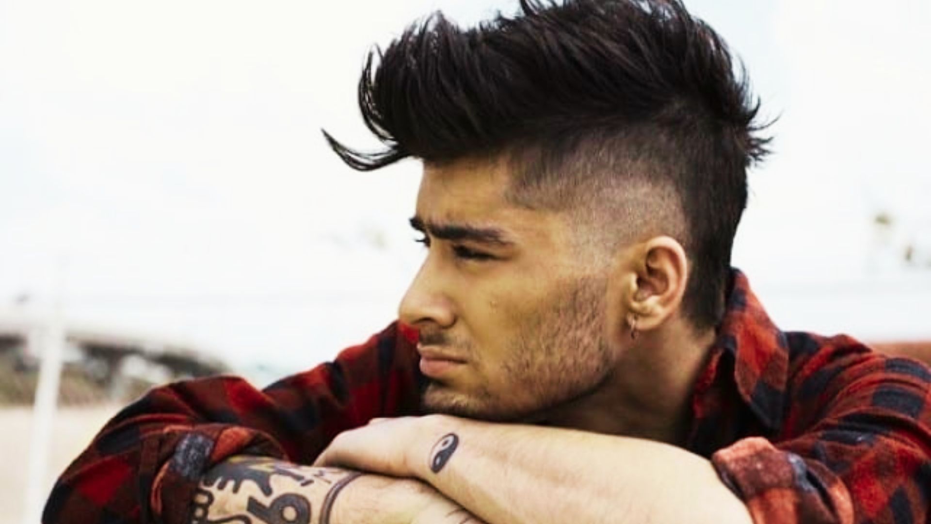 Zayn Malik with a tattoo on his arm sits on a bench, reflecting a casual style and interest in current hair trends.