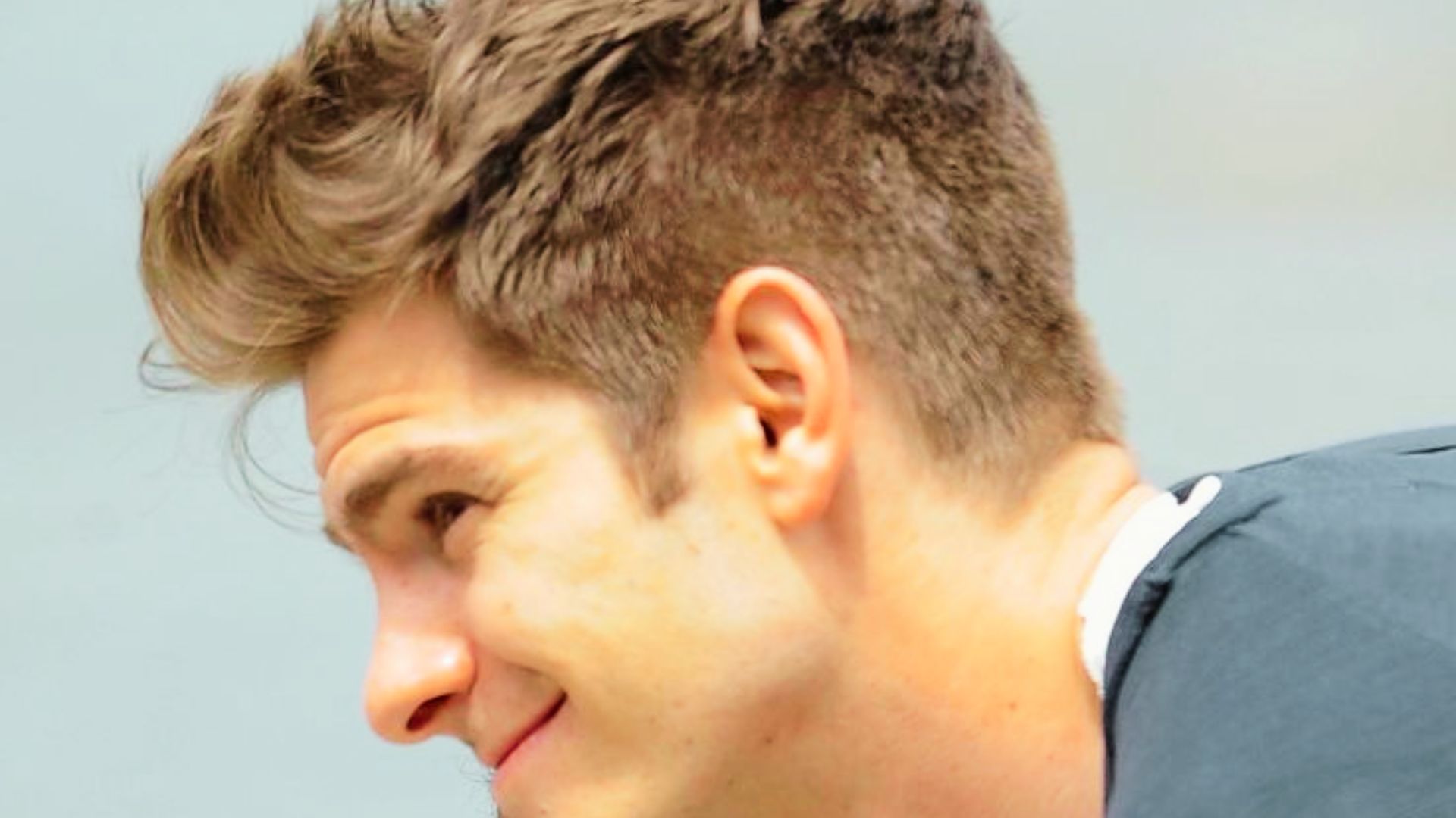 Andrew Garfield with a short haircut gazes thoughtfully