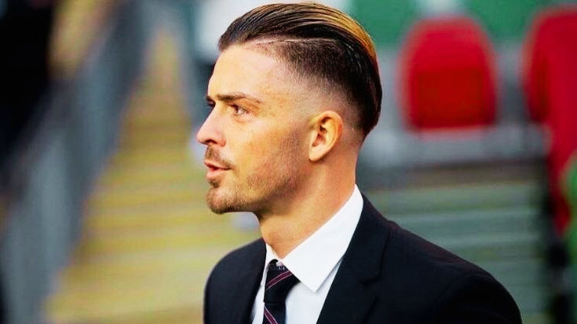 Jack Grealish in a suit and tie gazes away from the camera.