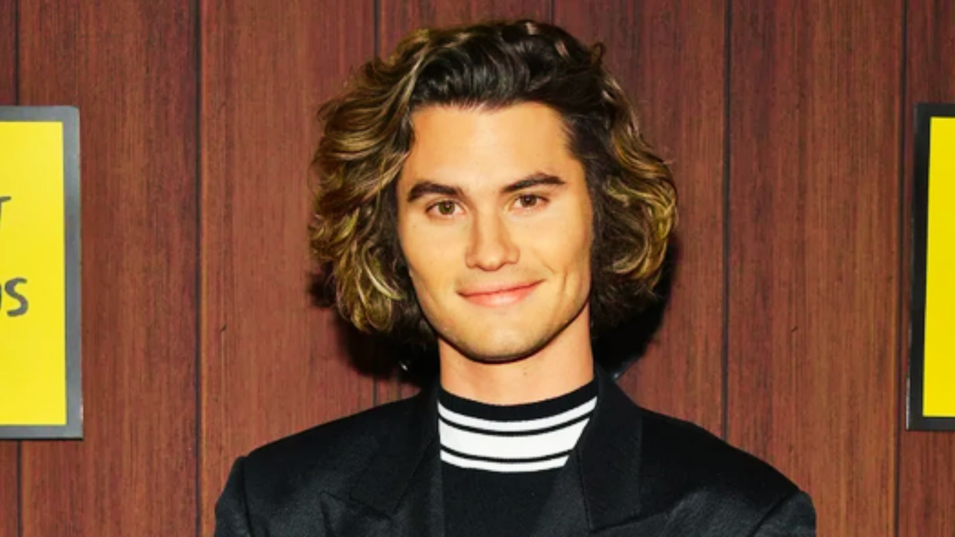 A man with long hair wearing a black jacket, showcasing a stylish and modern look.