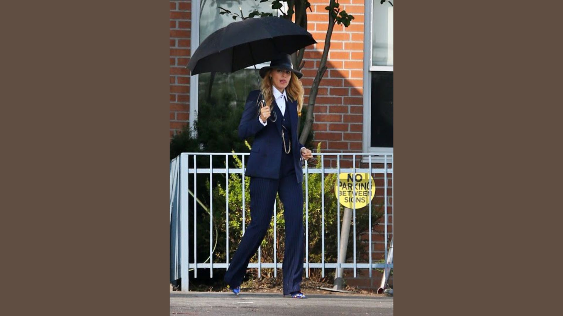 "A woman in a suit and high heels holds an umbrella, standing confidently against a neutral background."