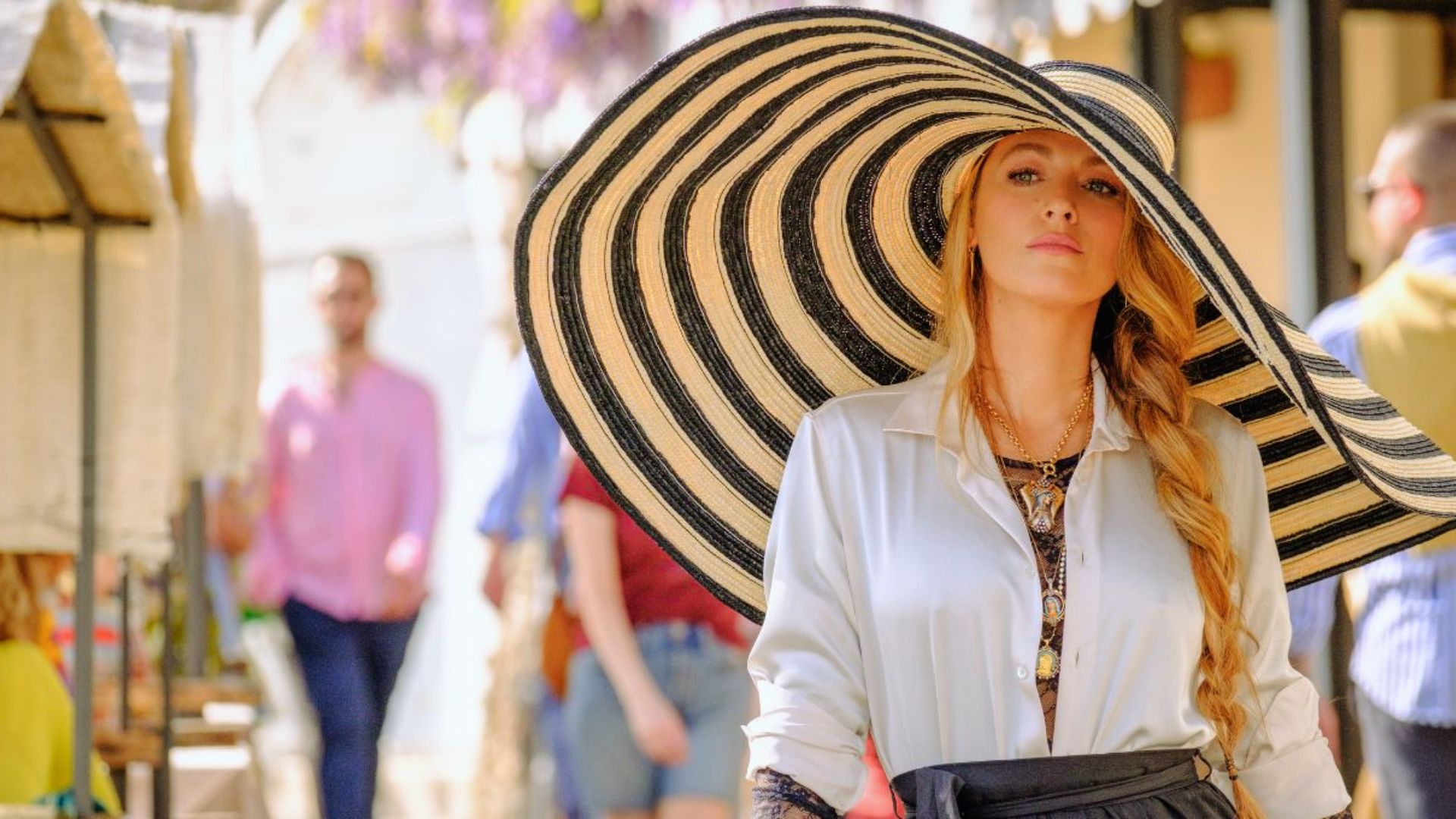 "A woman in a large hat browsing colorful stalls at a bustling market."
