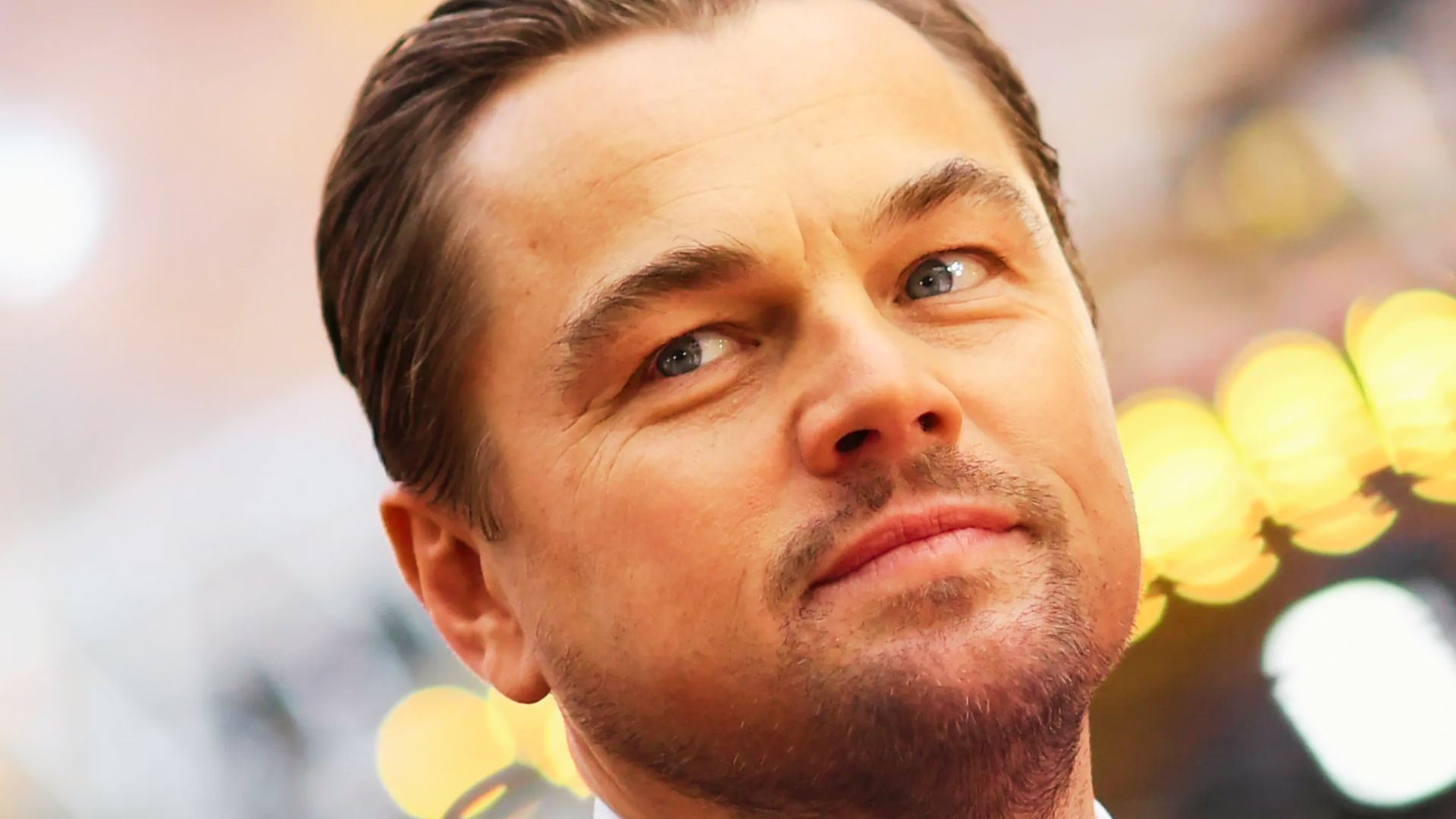 Leonardo DiCaprio at a red carpet event with a classic side-part hairstyle. Hair is slicked back neatly with a glossy finish, paired with a short boxed beard.