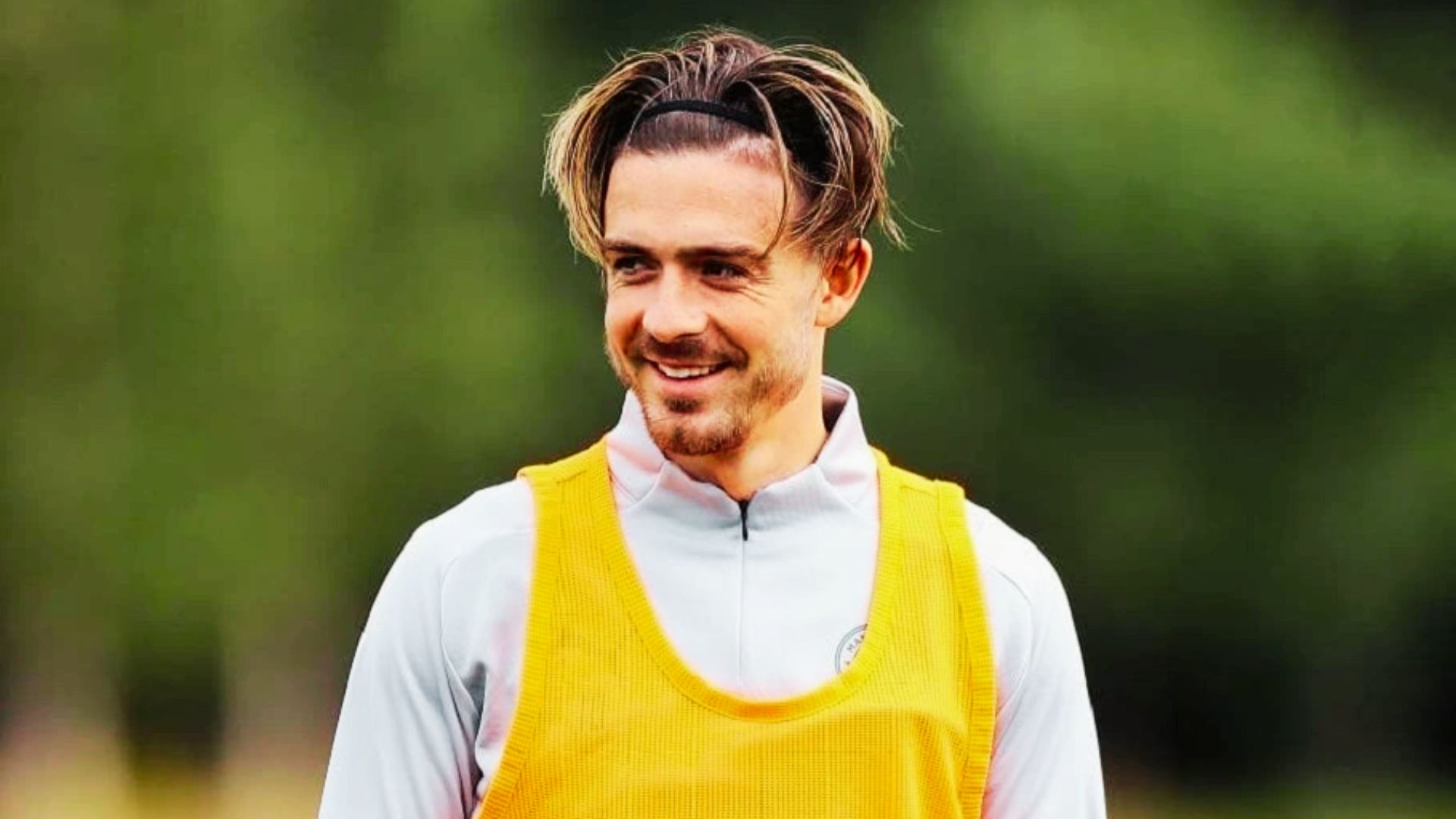 Jack Grealish with a ponytail smiles, showcasing the haircut style.