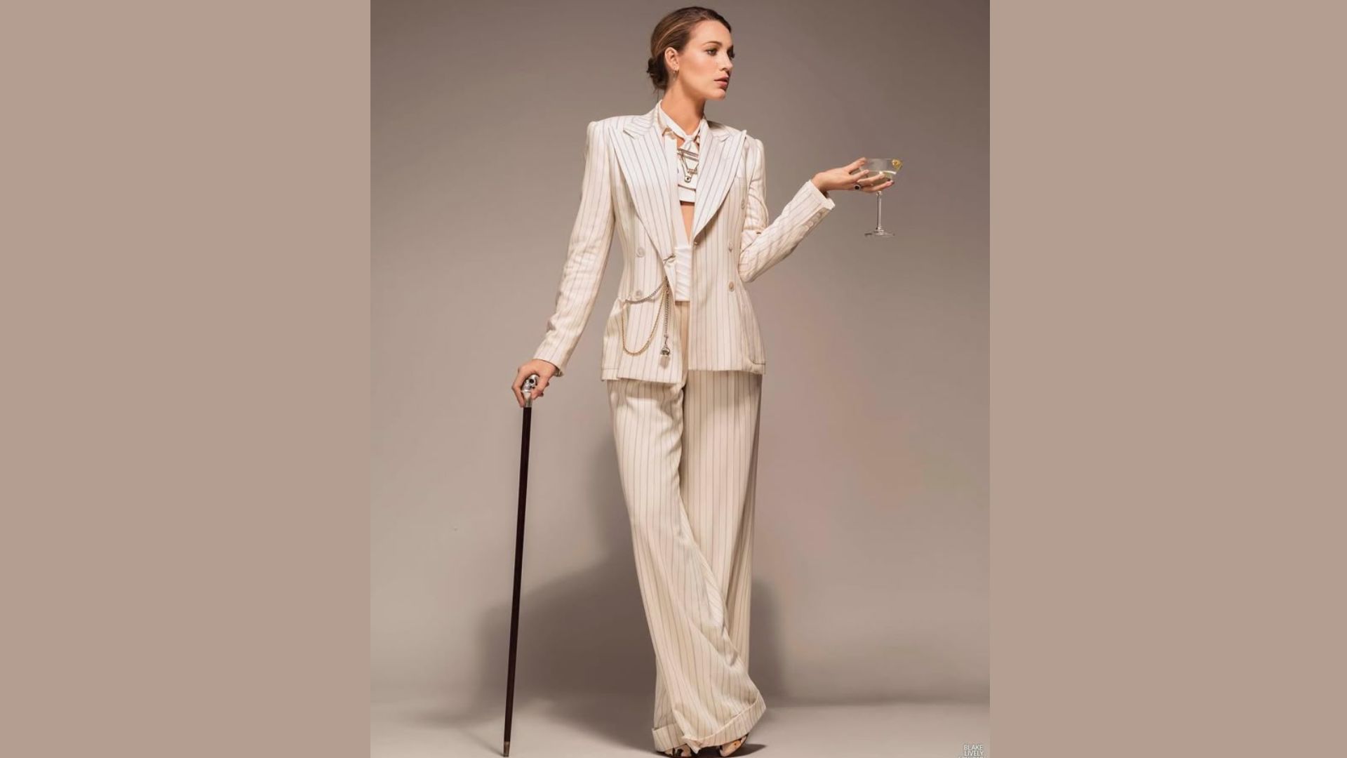 "A woman in a white suit and hat stands confidently, holding a cane in her right hand."