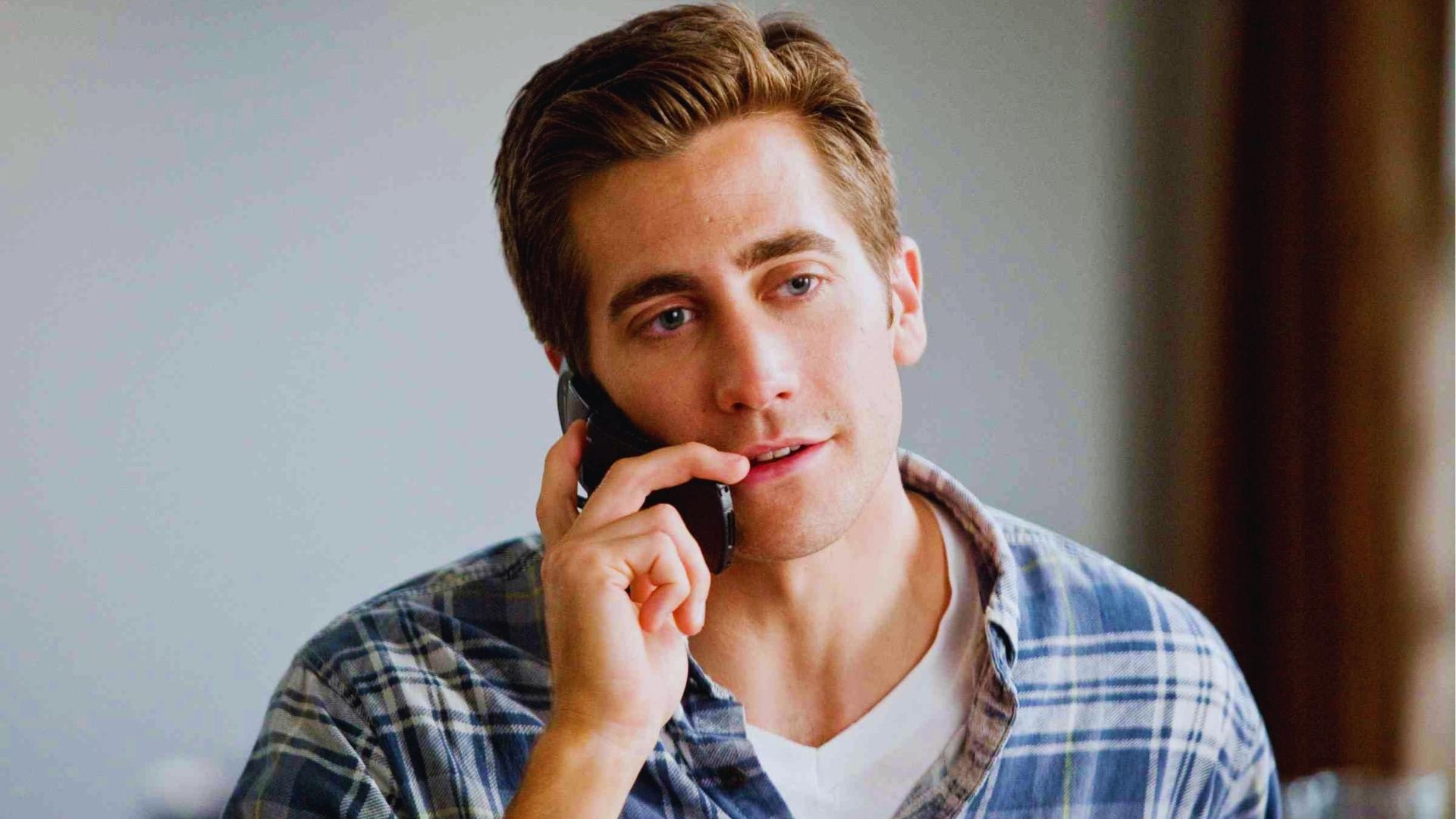 Young Jake Gyllenhaal on phone with classic short side-part haircut featuring tapered sides and combed-over top in plaid shirt.