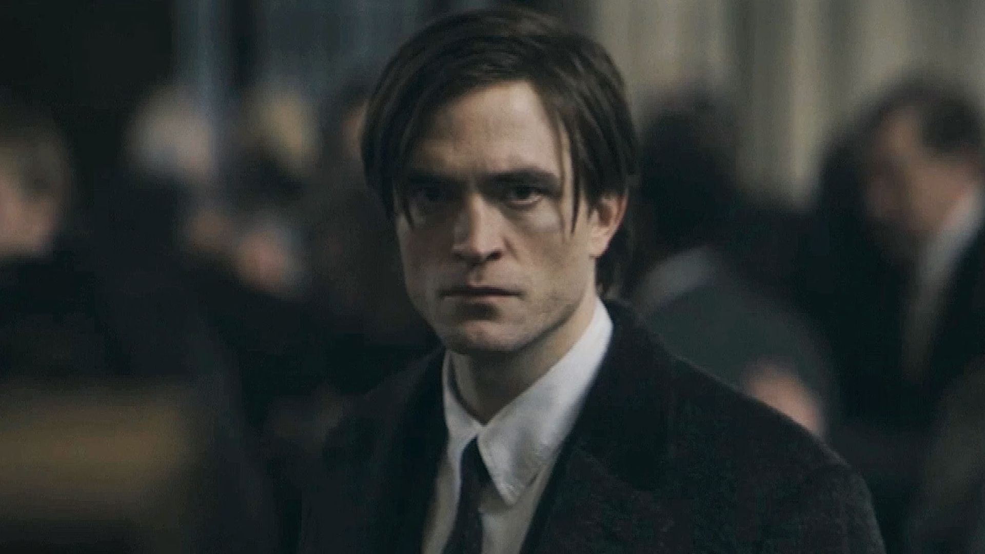 Robert Pattinson with long hair in black suit and tie.