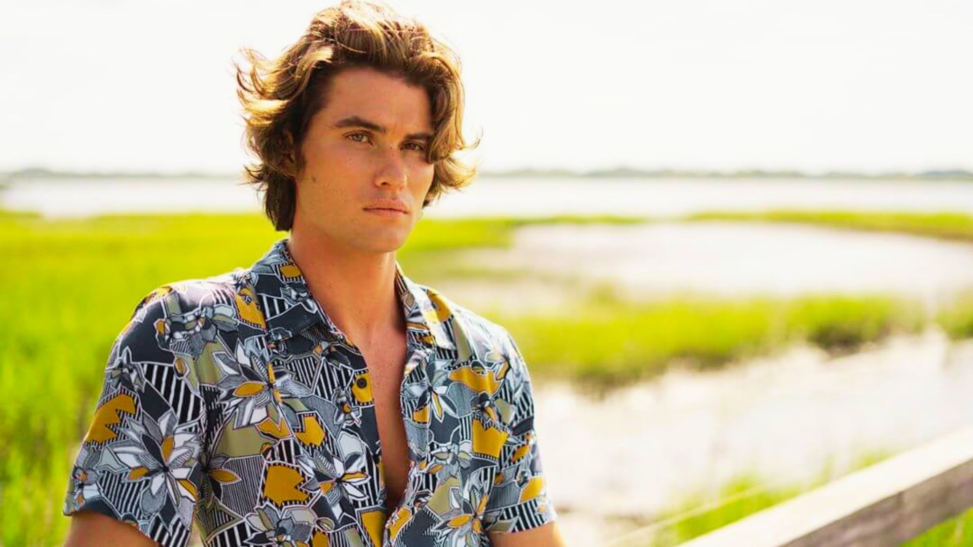 John B with long hair wearing a colorful floral shirt, demonstrating a casual summer style.