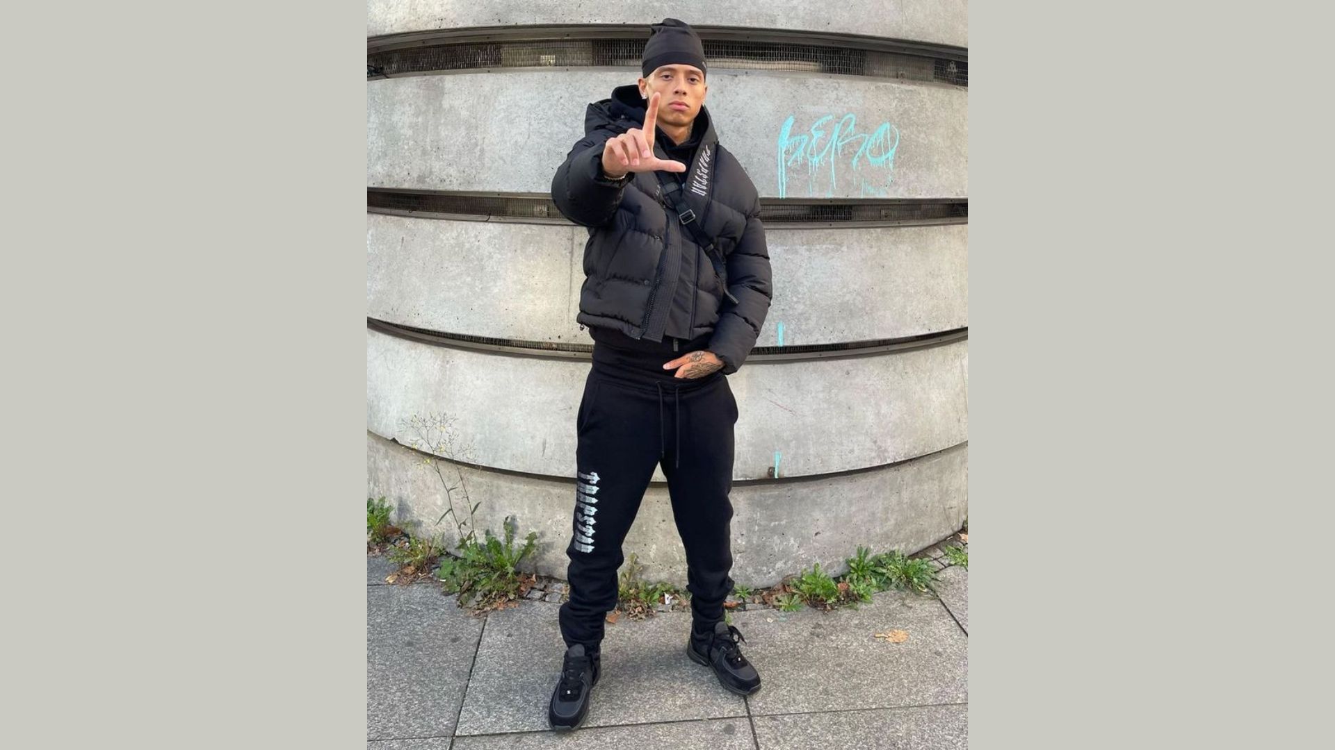 "A man dressed in a black jacket and pants gestures with his right hand while appearing engaged in conversation."