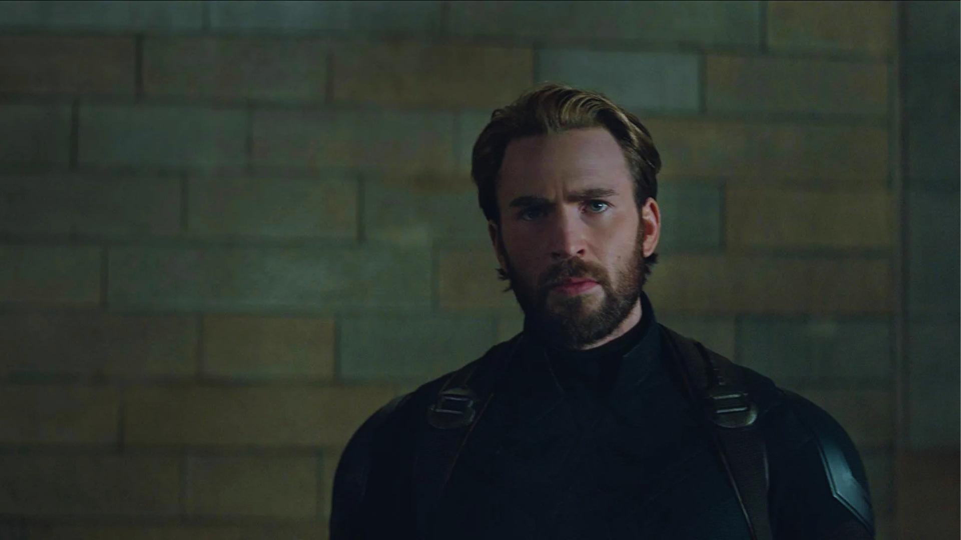 Chris Evans as Captain America with medium-length swept-back haircut, tapered sides, and full beard in dark tactical suit.