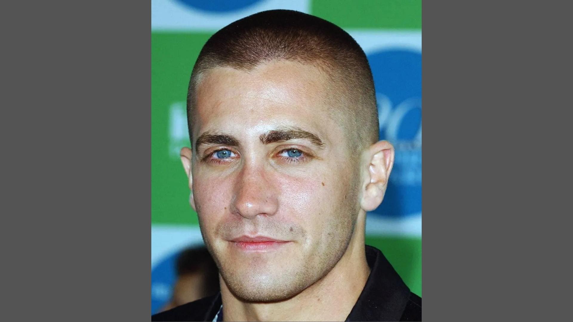 Jake Gyllenhaal with military buzz cut haircut and clean shave wearing black shirt at red carpet event.