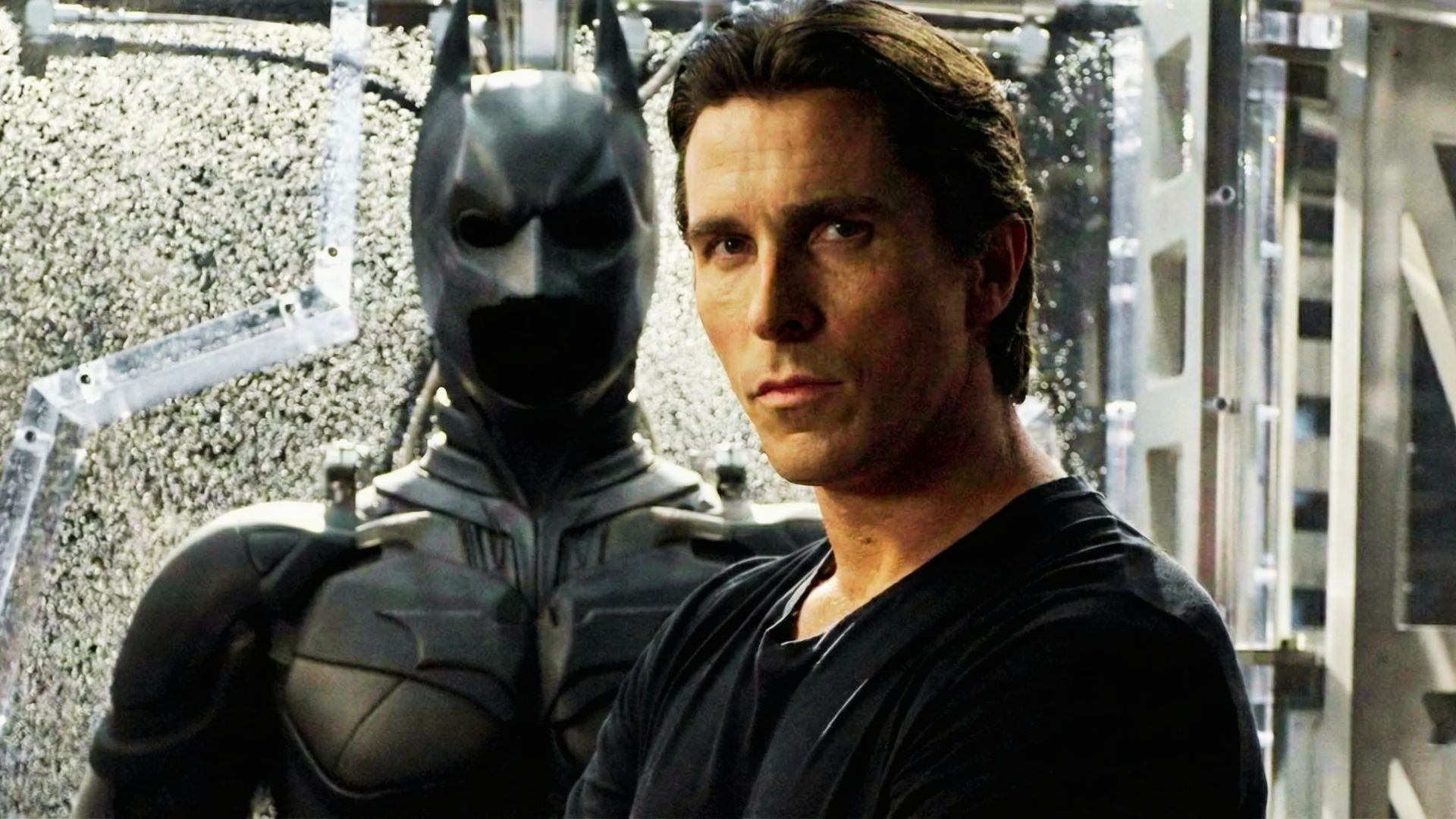 Batman, portrayed by Christian Bale,standing in front of the Batman suit intense scene from The Dark Knight Rises.