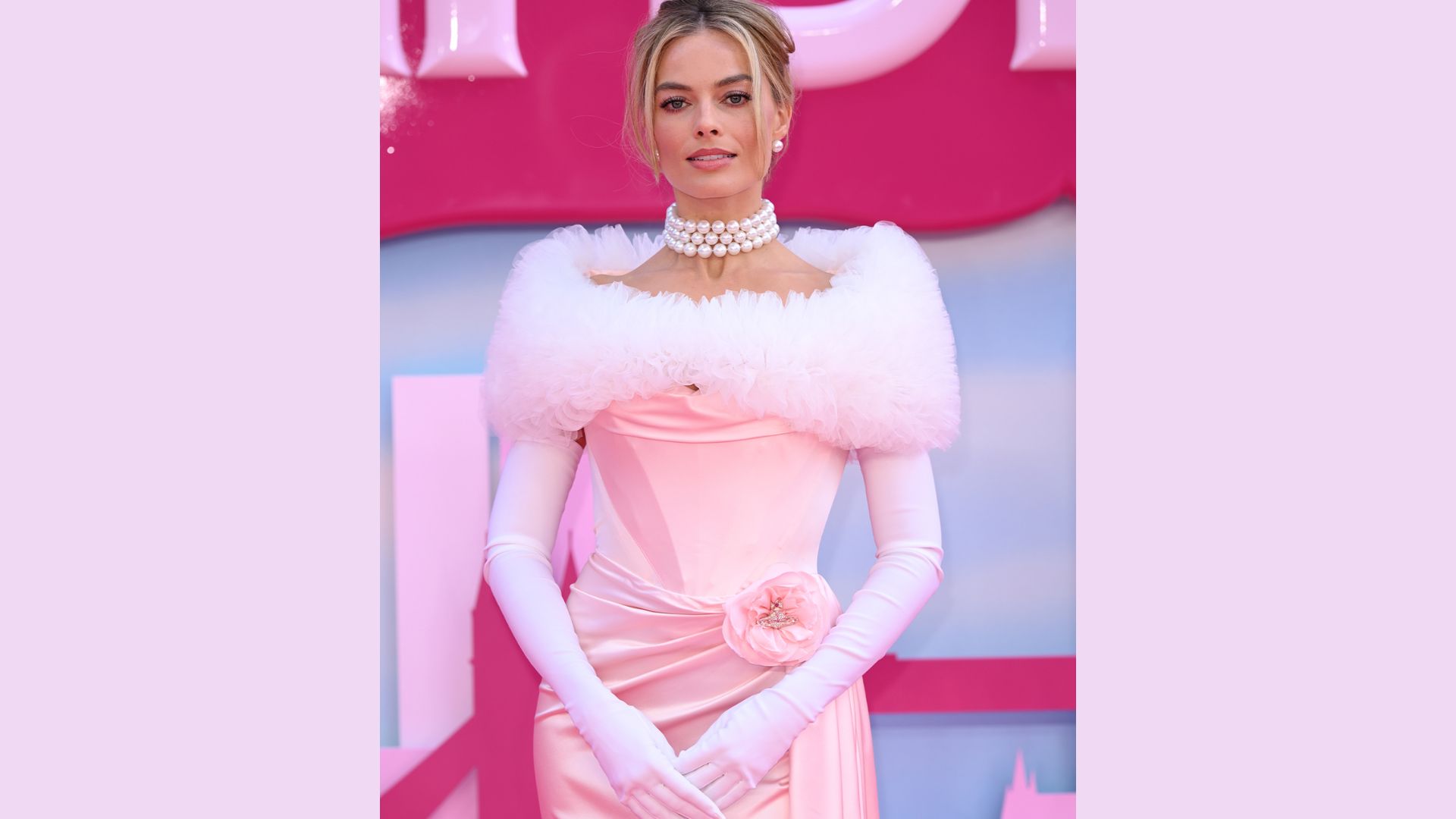 "A woman wearing a pink dress and a white fur stole stands gracefully with a soft smile and elegant posture."