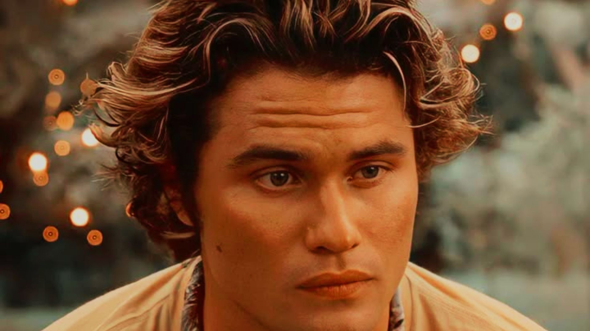 A man with long curly hair gazes directly at the camera