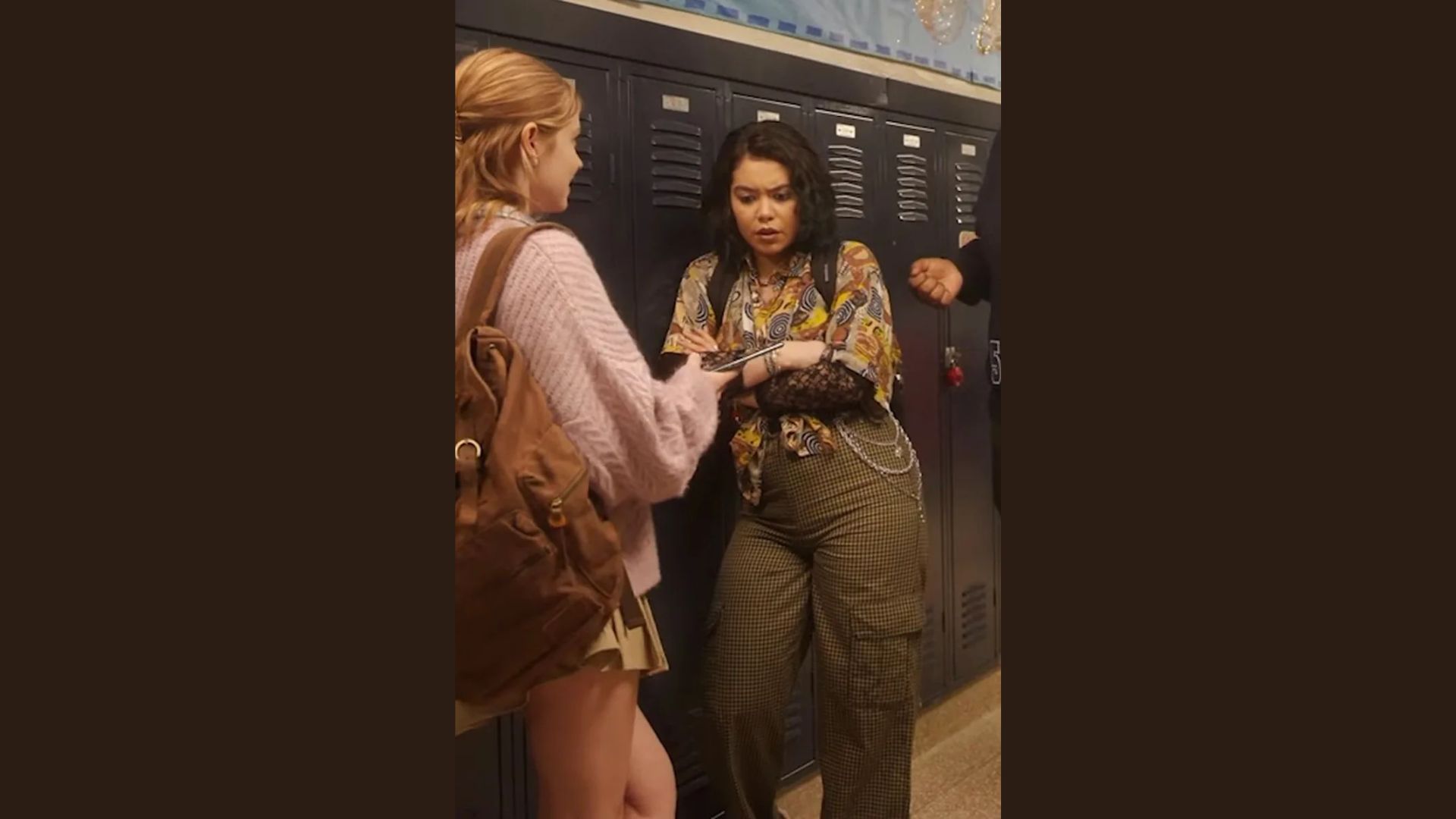"Two girls engaged in conversation while standing in a hallway, sharing smiles and animated expressions."