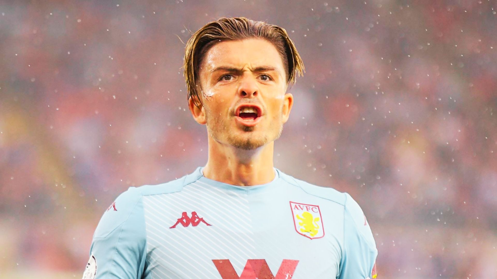 Jack Grealish in a blue shirt stands in the rain, showcasing a stylish haircut.