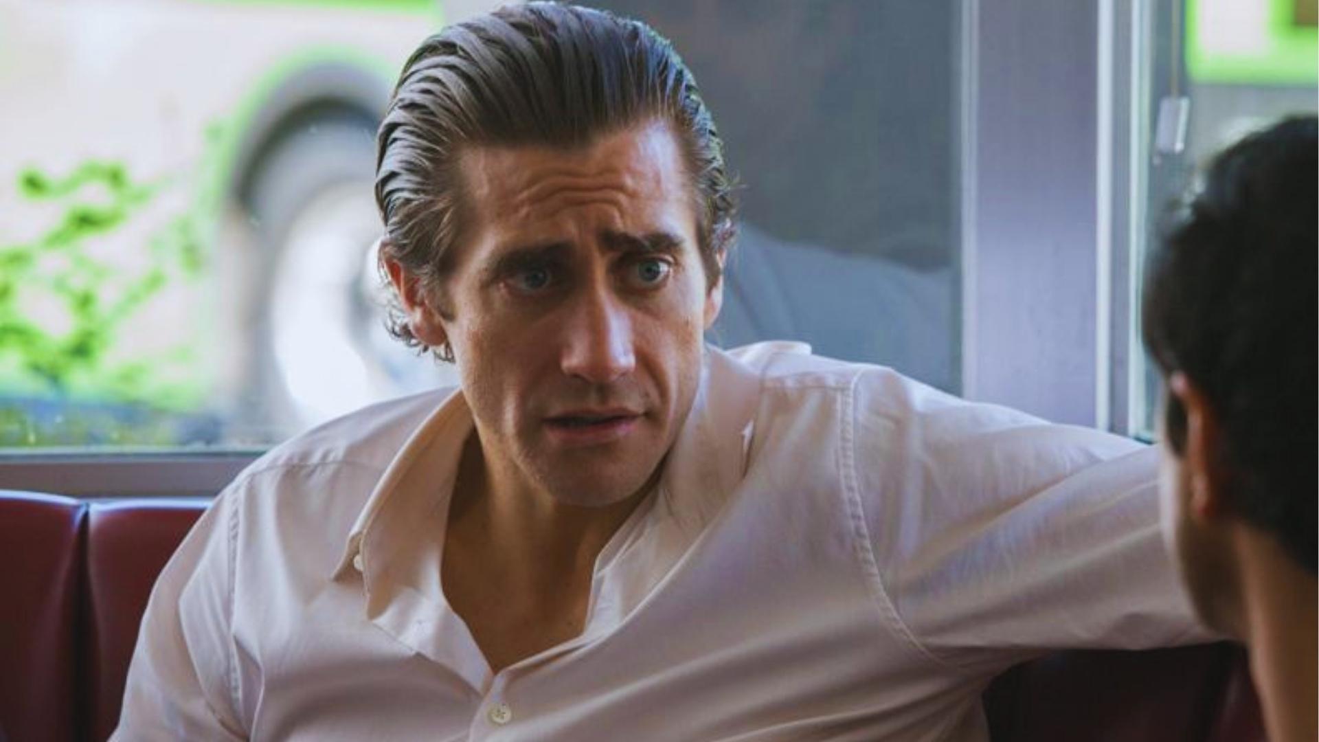 Jake Gyllenhaal with long slicked-back haircut wearing white shirt in diner scene.