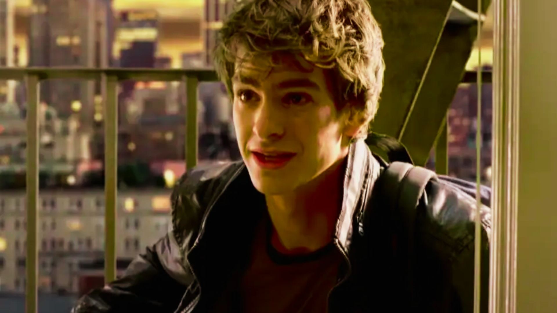 Andrew Garfield in a black jacket sits on a balcony, in his Peter Parker's look.