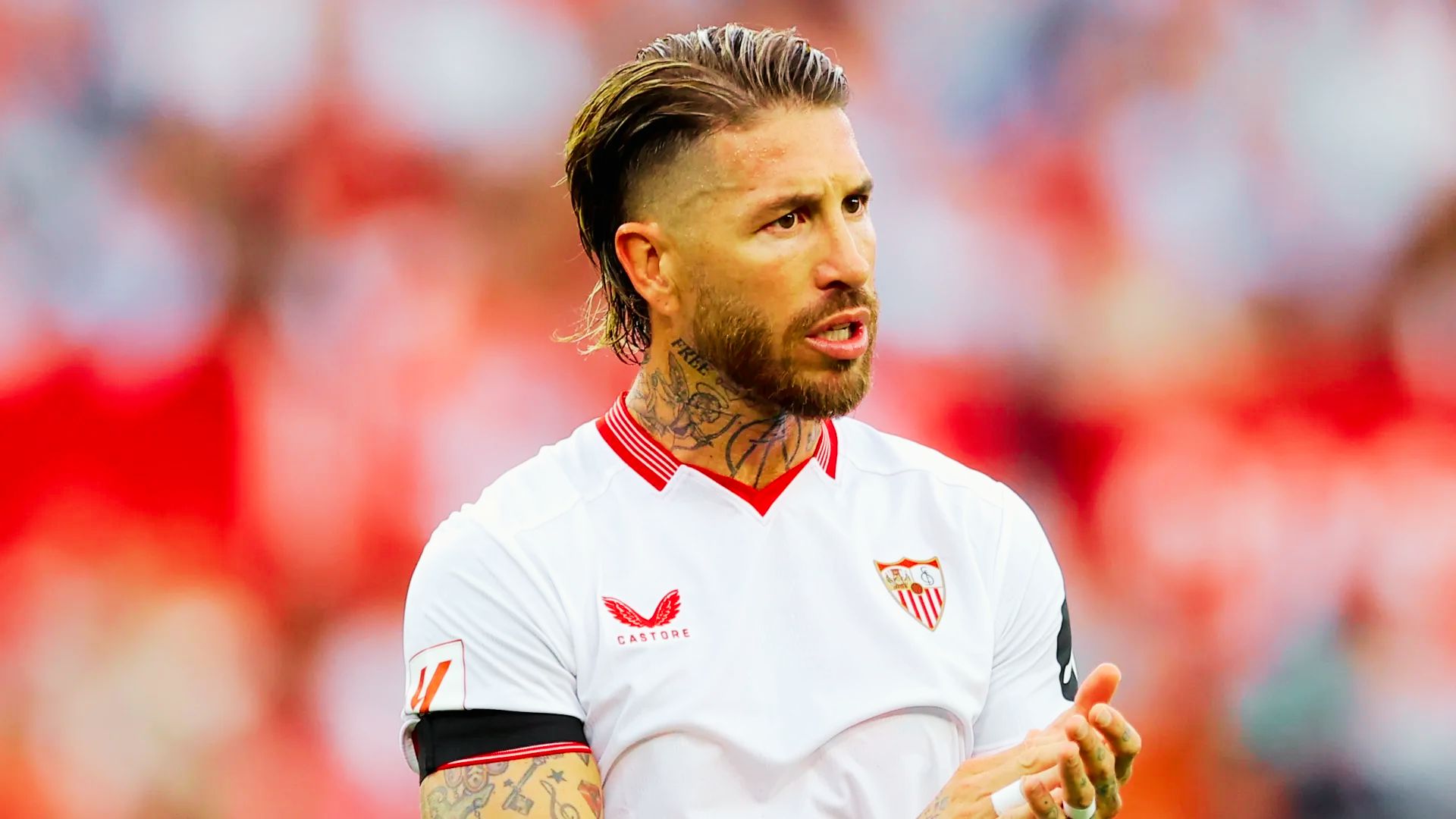 Sergio Ramos with tattoos on his arm stands confidently on a vibrant soccer field, ready for action.