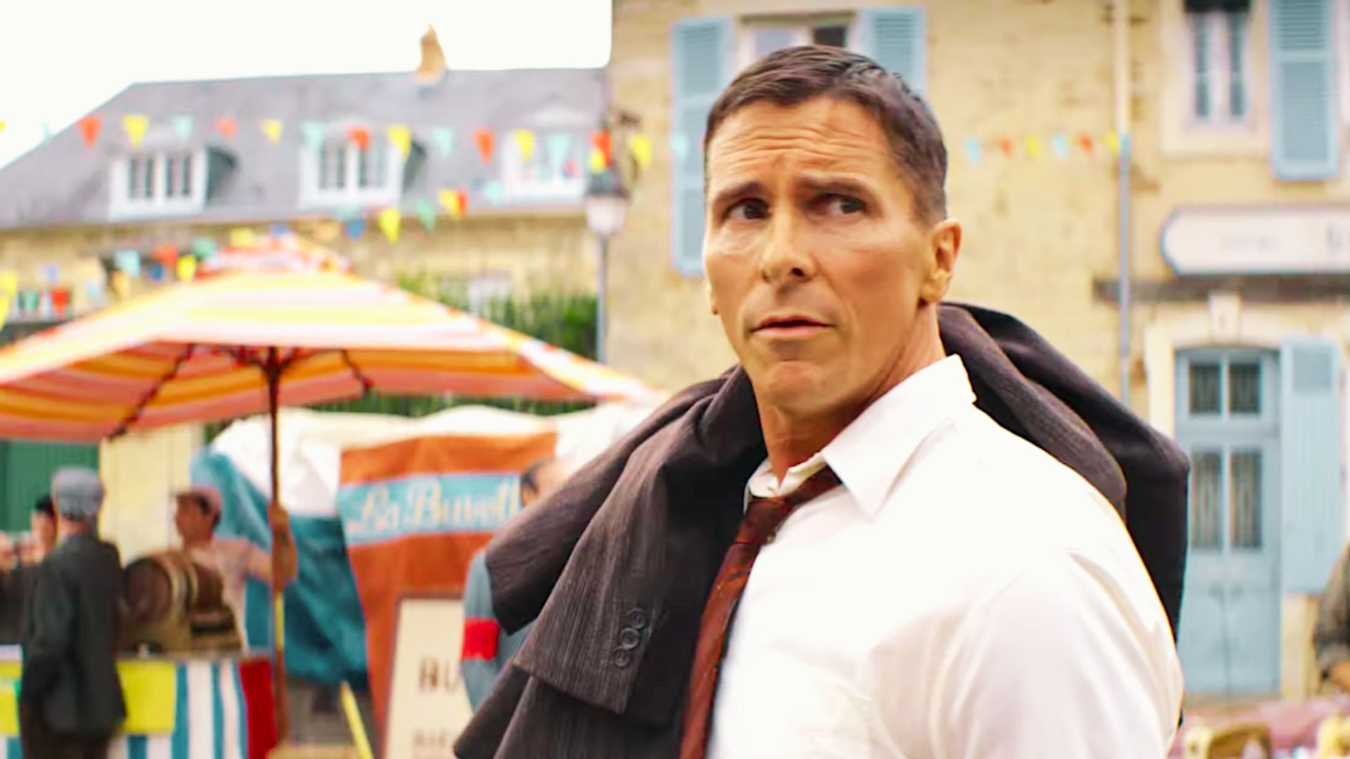 Christian Bale in a white shirt and tie stands confidently in front of an engaged crowd.