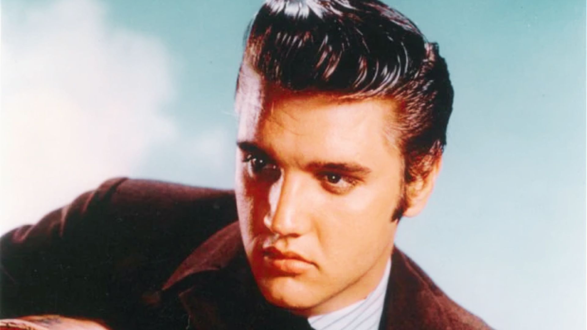 Elvis Presley in a suit and tie, showcasing a clean look with his short haircut, exuding classic style and charisma.