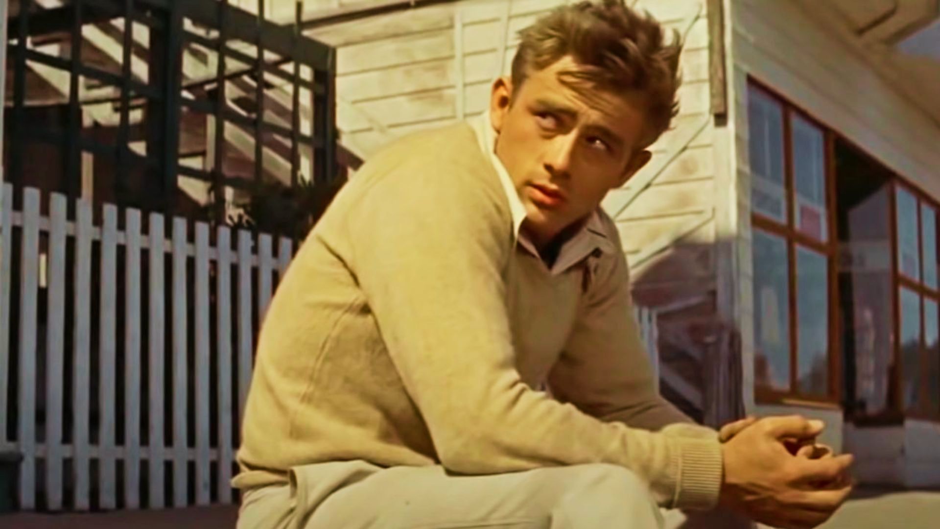 James Dean haircut for Everyday Style sits on the ground, hands resting on his knees, looking relaxed and stylish.