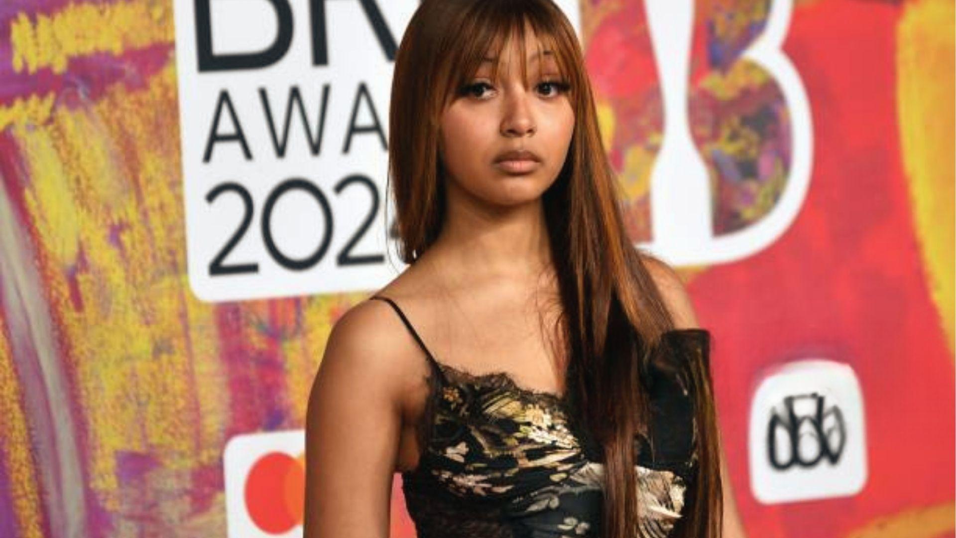 PinkPantheress at BRITs 2024 in black lace floral corset with off shoulder strap.
