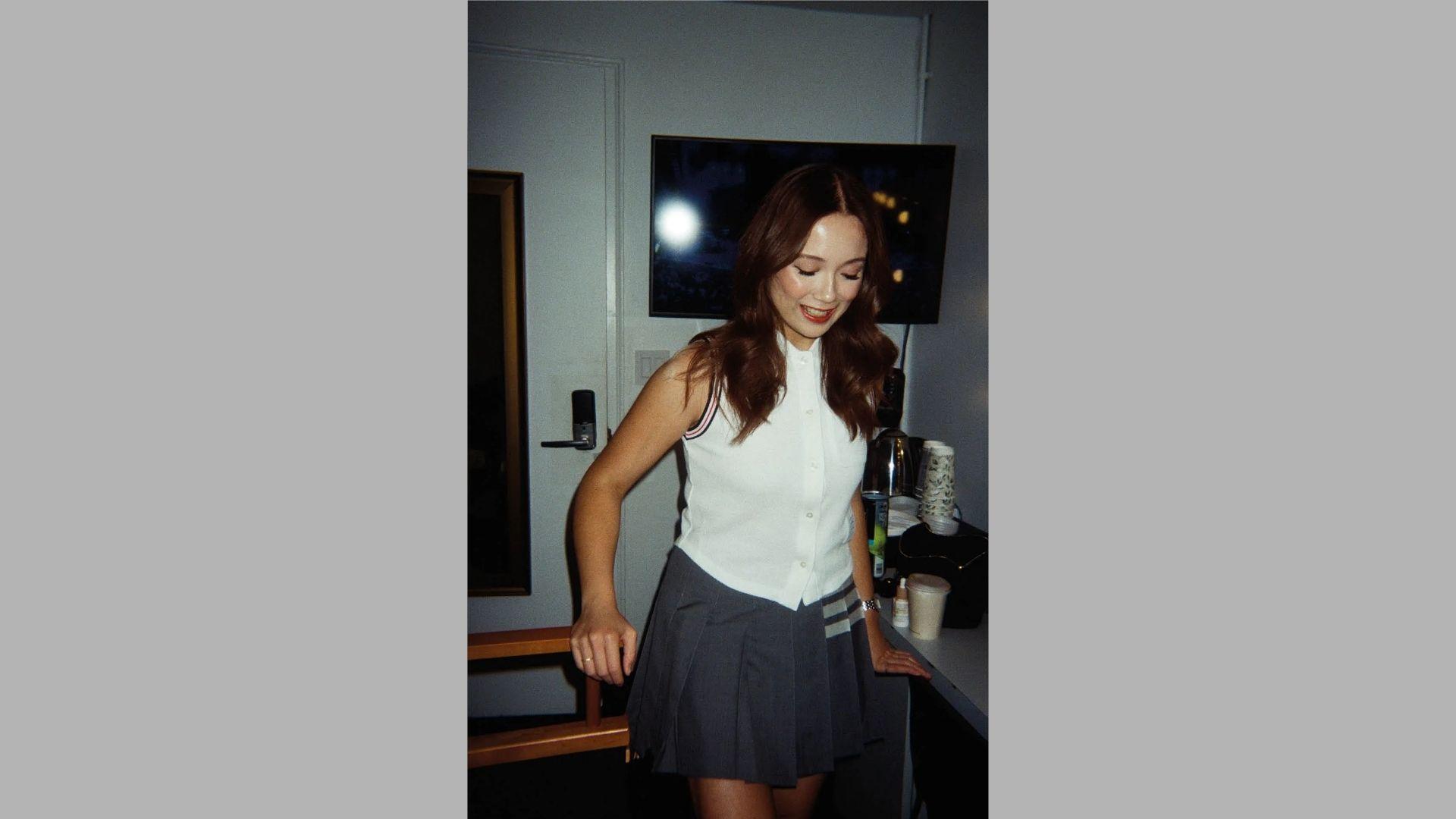 Woman laughs wearing white sleeveless top and pleated skirt leaning by kitchen counter at night