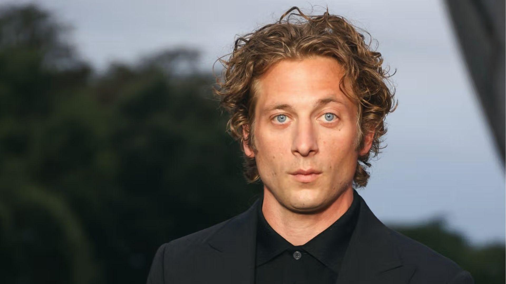 Jeremy Allen White has medium-length messy blonde curls with natural volume in outdoor black suit photo