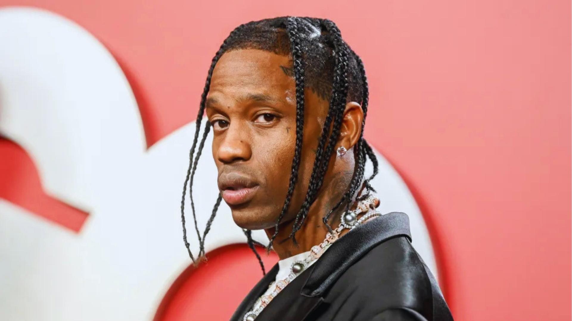 Travis Scott on the red carpet with long, thin box braids, a sharp hairline shape-up, and layered diamond necklaces.