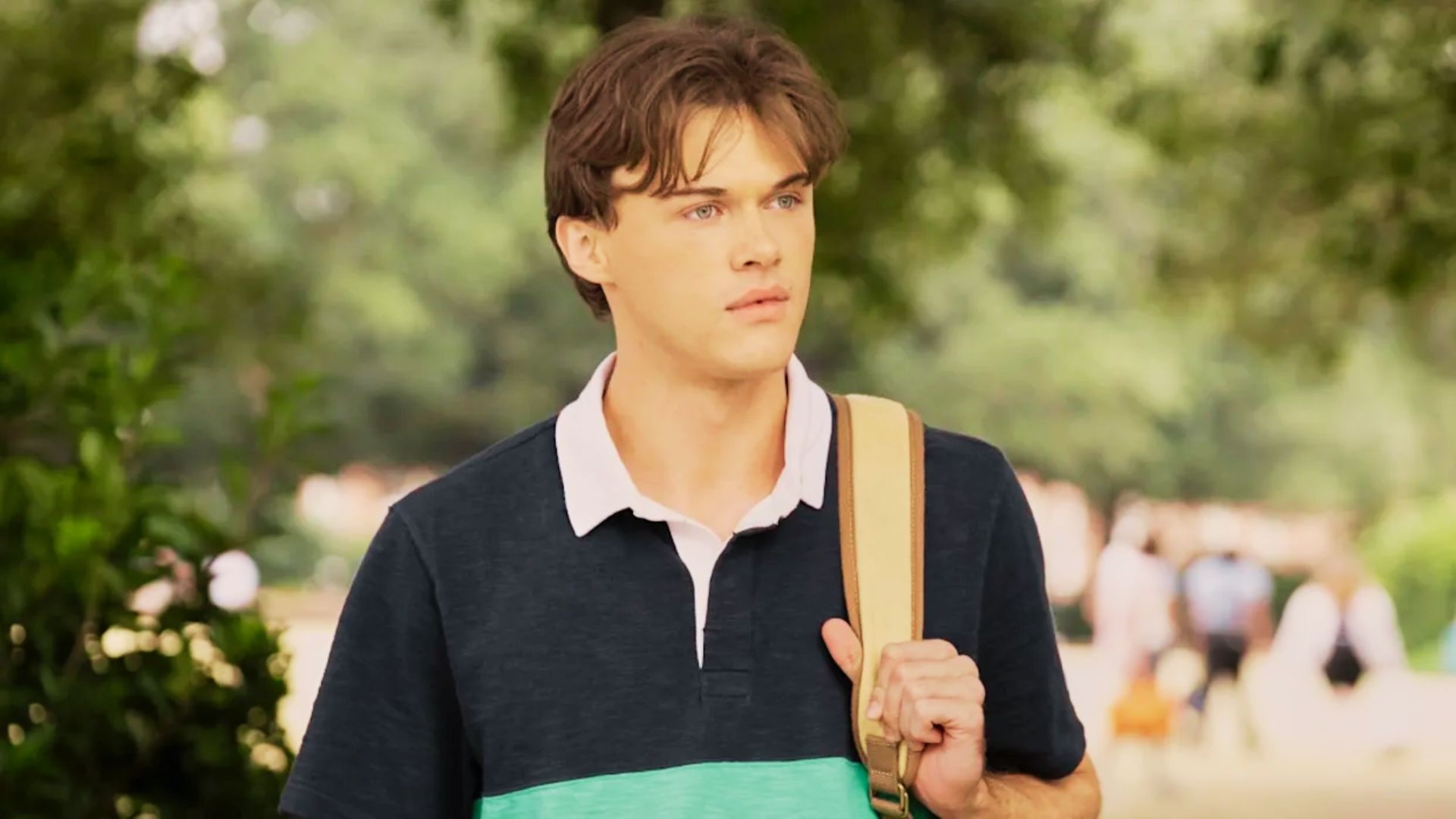 Conrad wears a navy and green colorblock polo with a tan backpack on a sunny street.