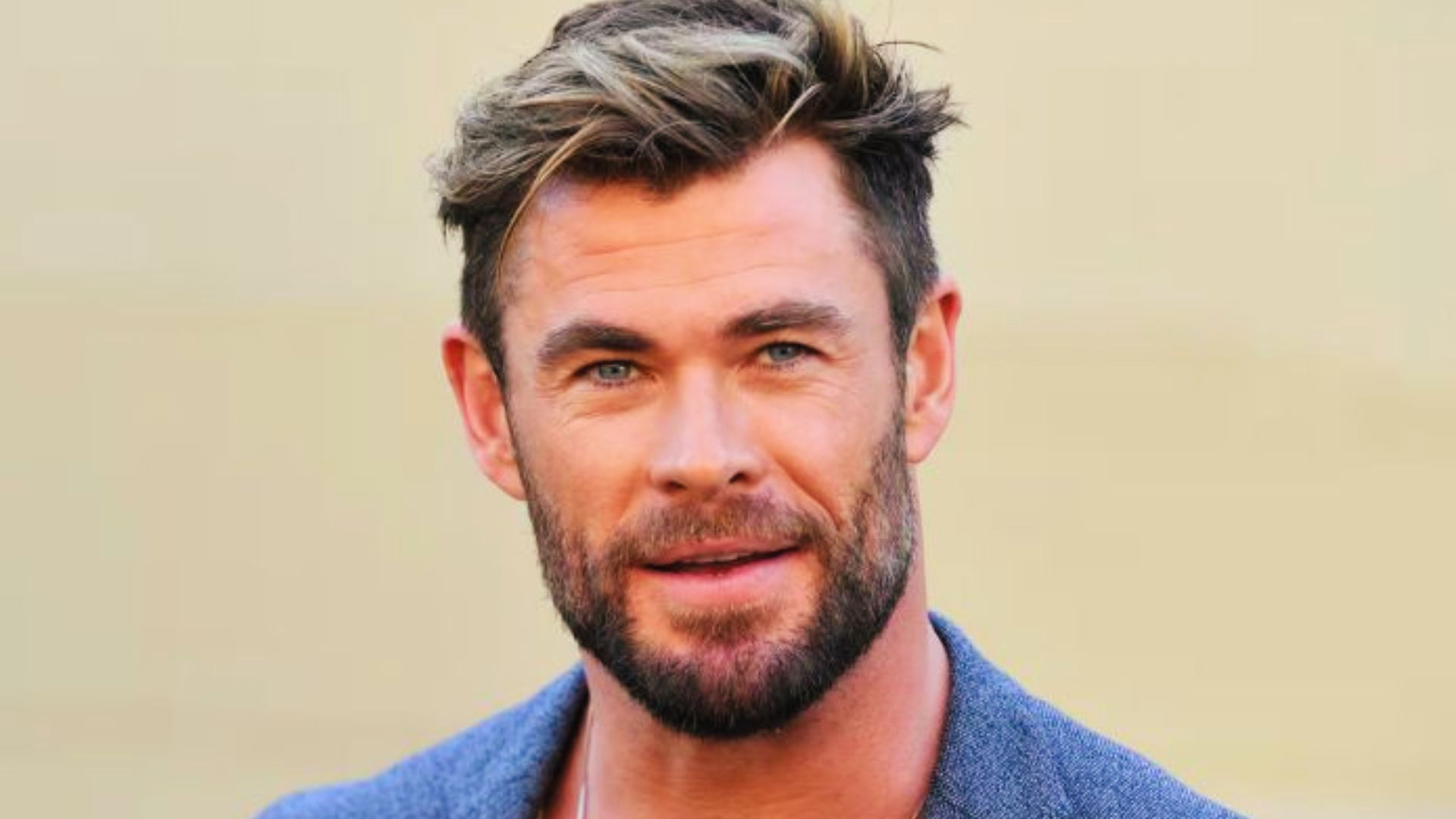 man with a beard wearing a blue shirt, showcasing a Chris Hemsworth-inspired brushed back hairstyle.