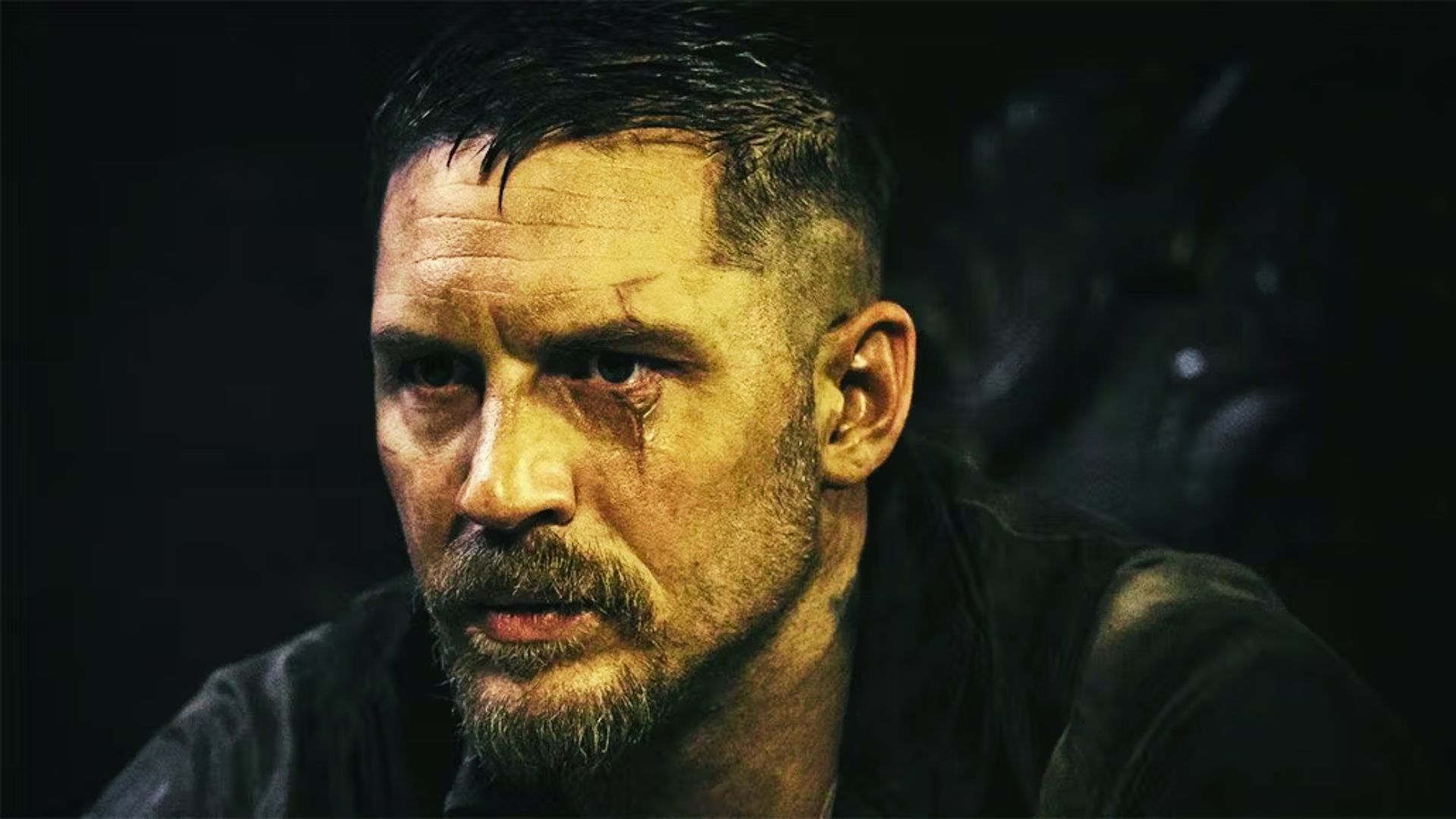 Tom Hardy sporting a short textured crop with shaved sides and a full rugged beard.