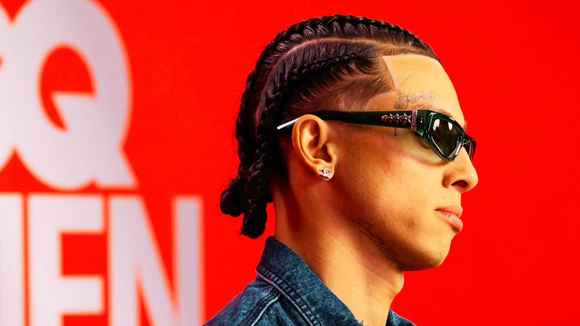 Side view of Central Cee at a GQ event, showing neat cornrows styled into a low bun with shaved line details.
