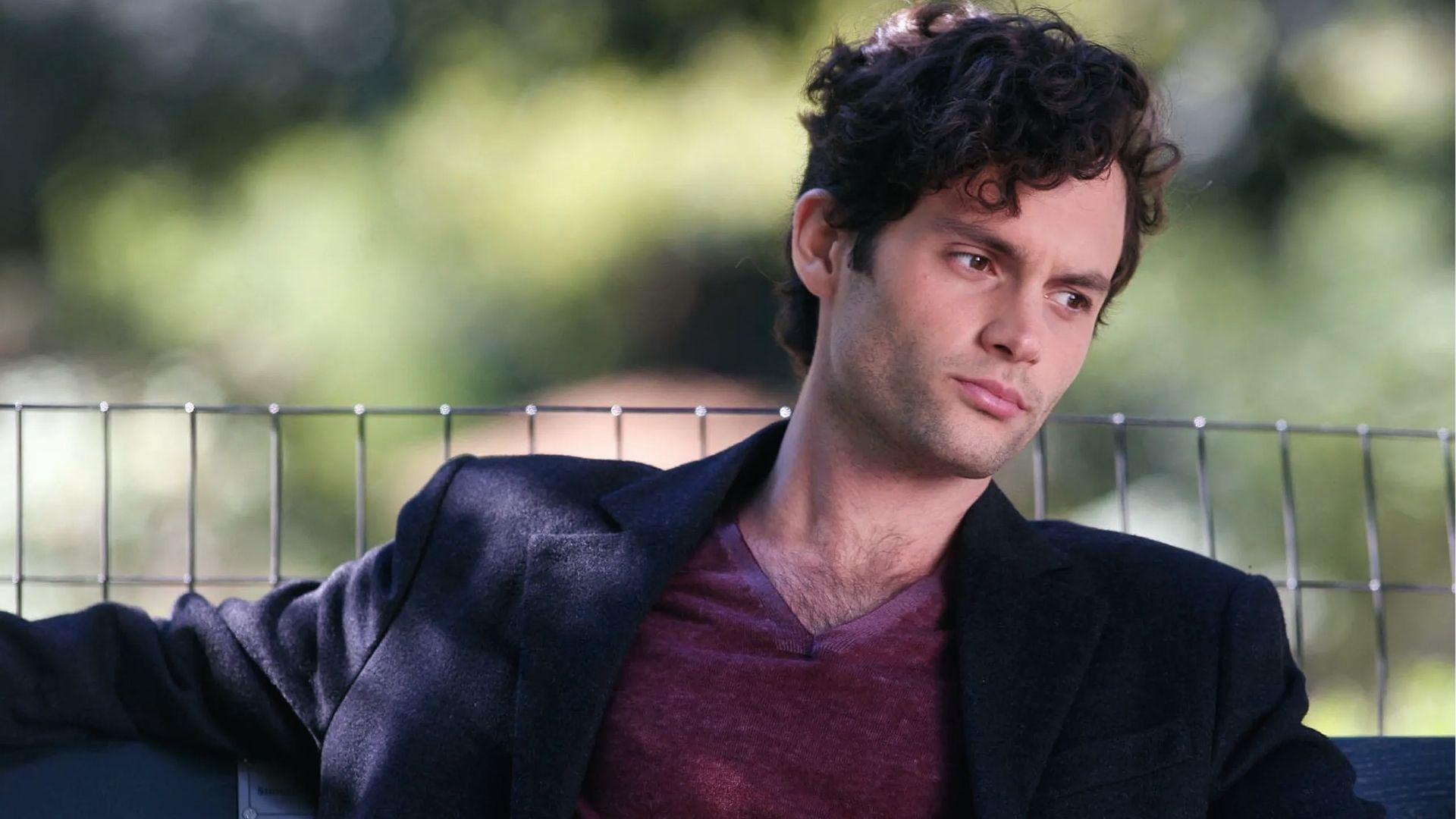 Penn Badgley displays casual Short Curly Hairstyle with Soft Quiff sitting outdoors in a blazer look.