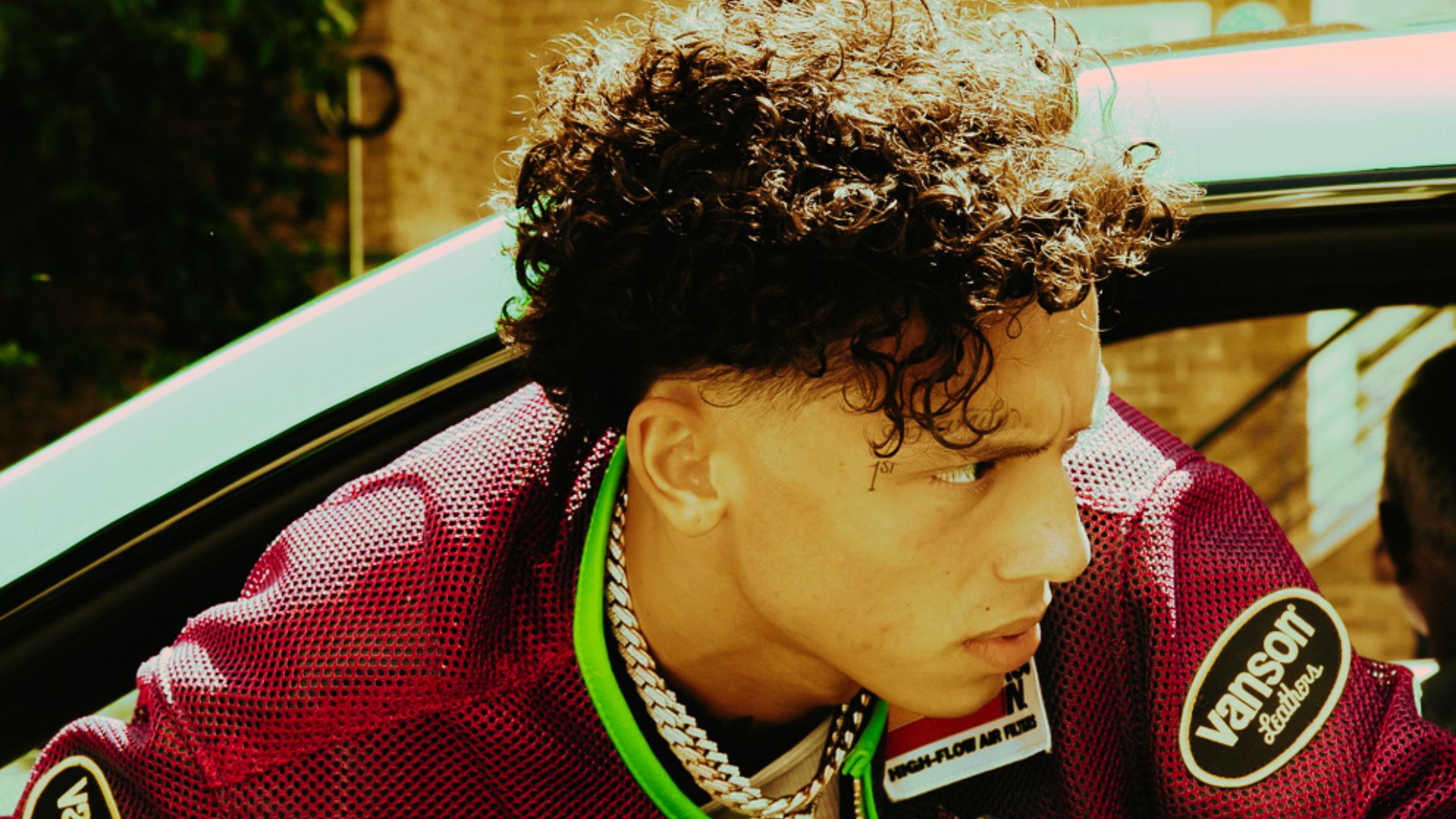 Side profile of Central Cee leaning out of a car, displaying his curly hair with a clean mid fade.